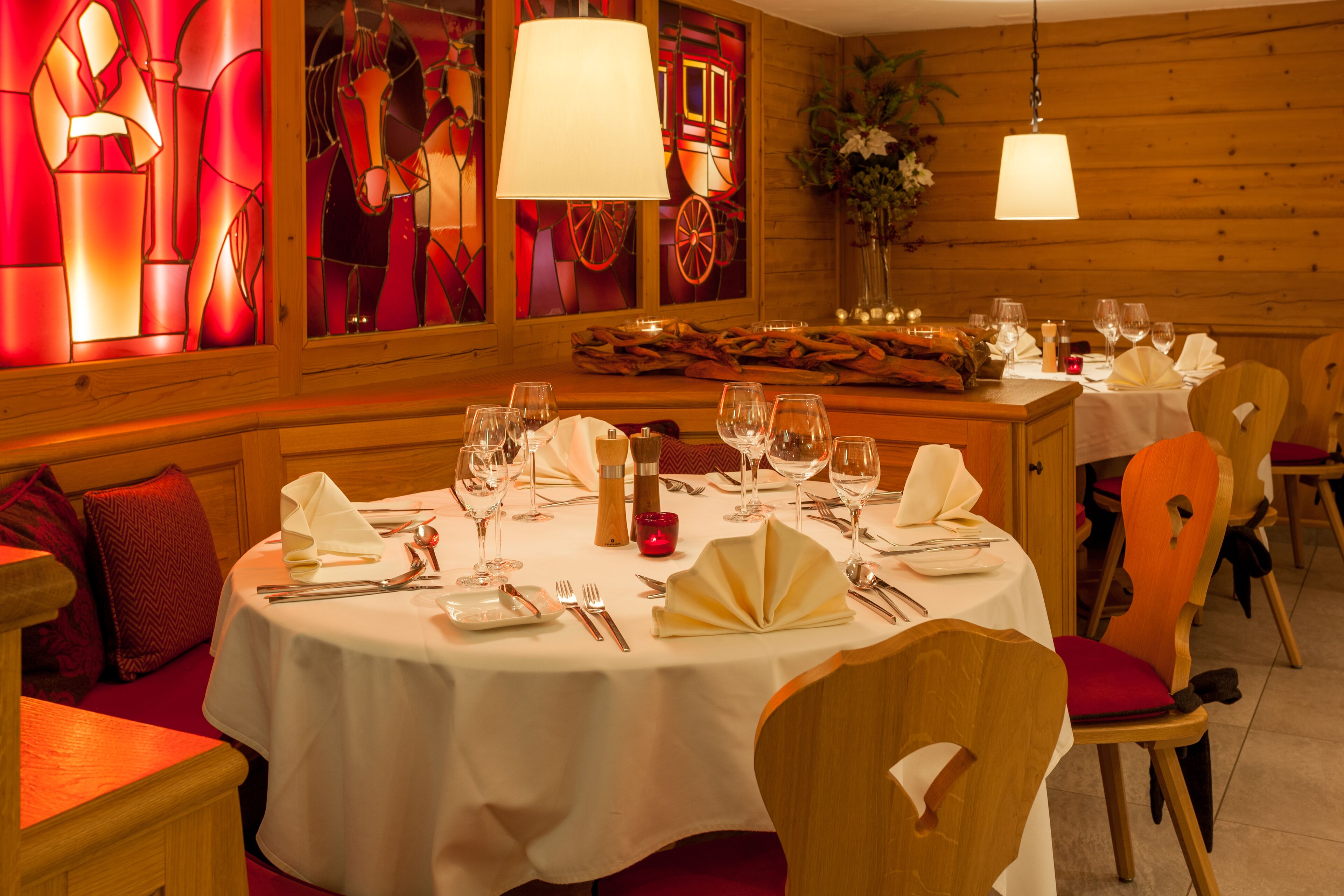 Een restaurant met ronde tafels gedekt voor diner, houten stoelen en een warme sfeer dankzij houten wanden en glas-in-loodramen.