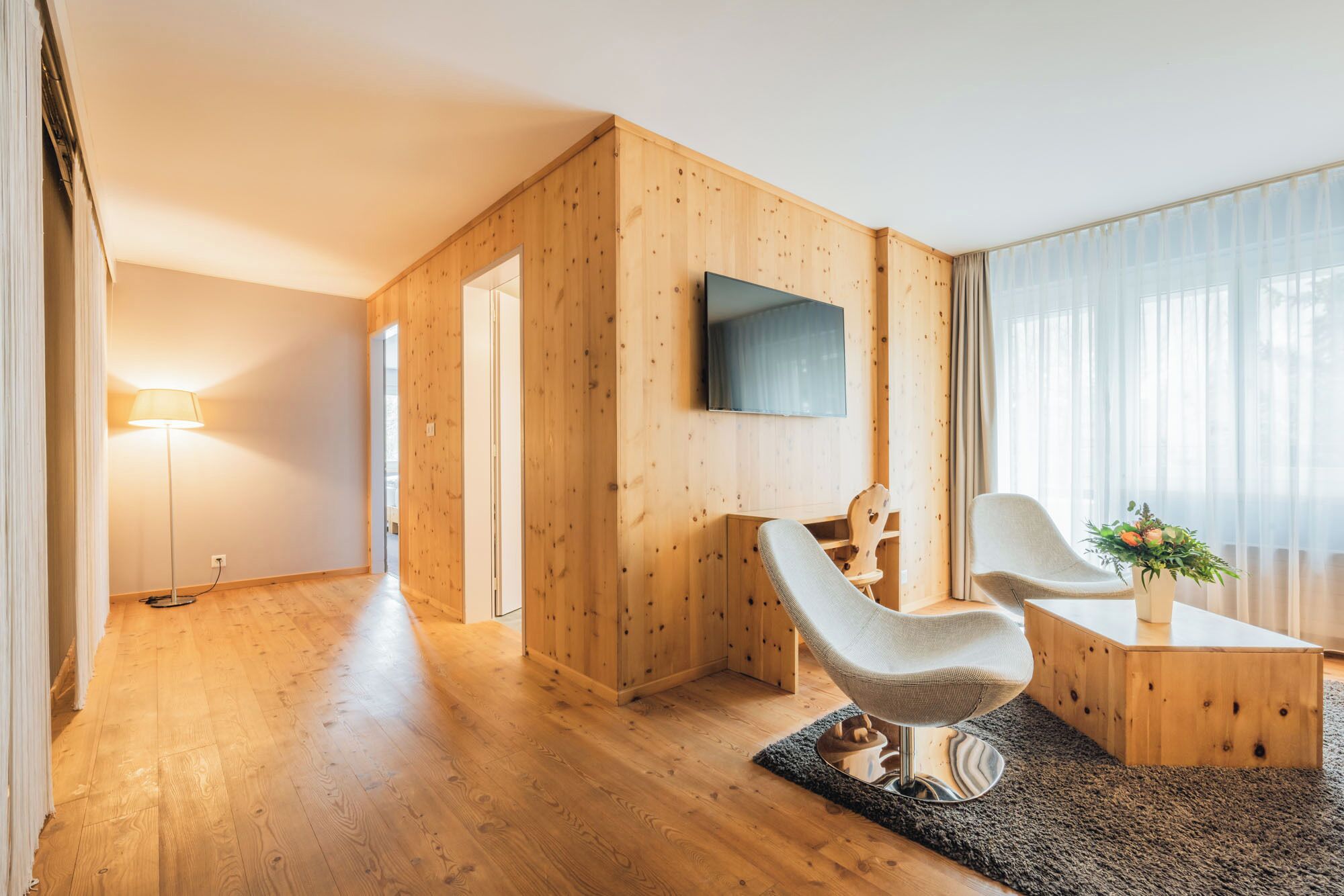 Un salon moderne avec des murs en bois, un téléviseur à écran plat, deux fauteuils, une petite table et une lampe.