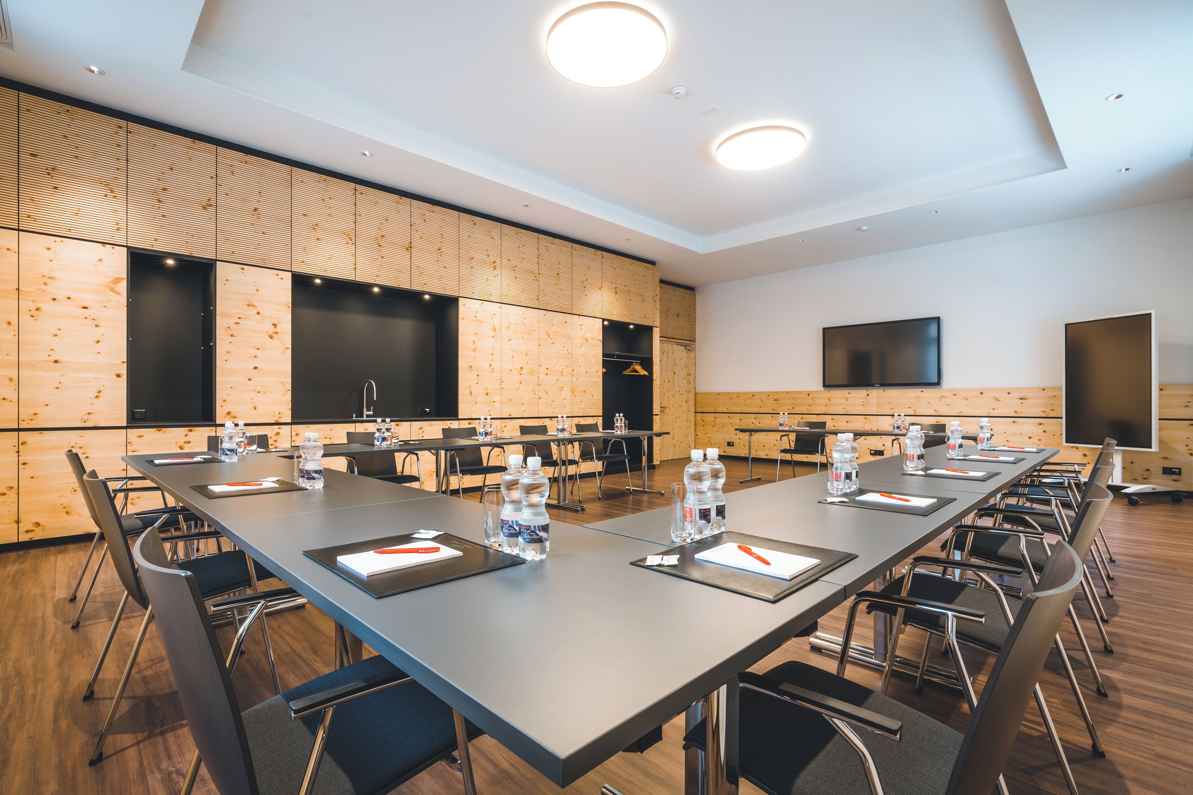 A conference room with a long table, chairs, water bottles, and a flat-screen TV.