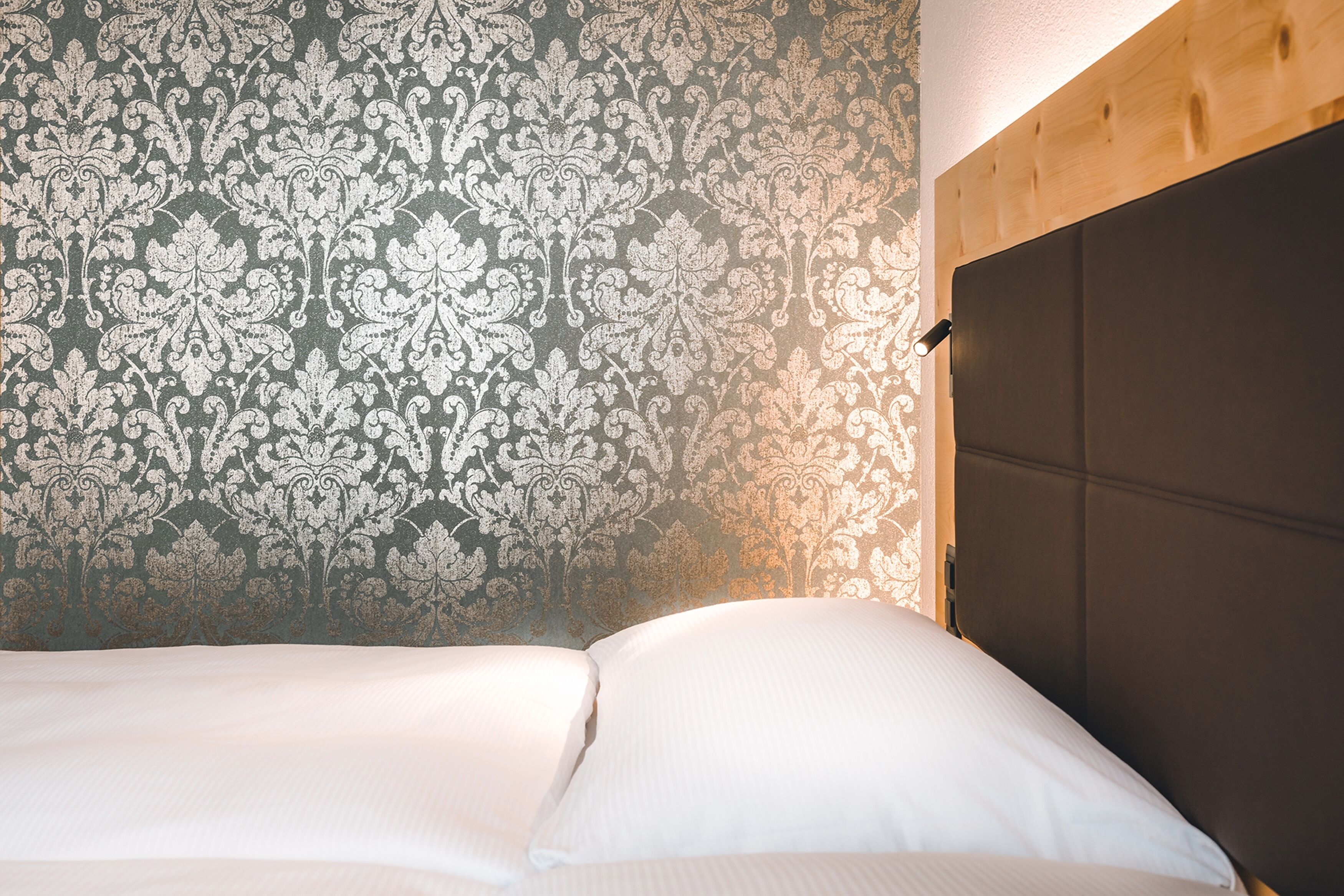 A bed with white linens and a patterned wallpaper in the background.