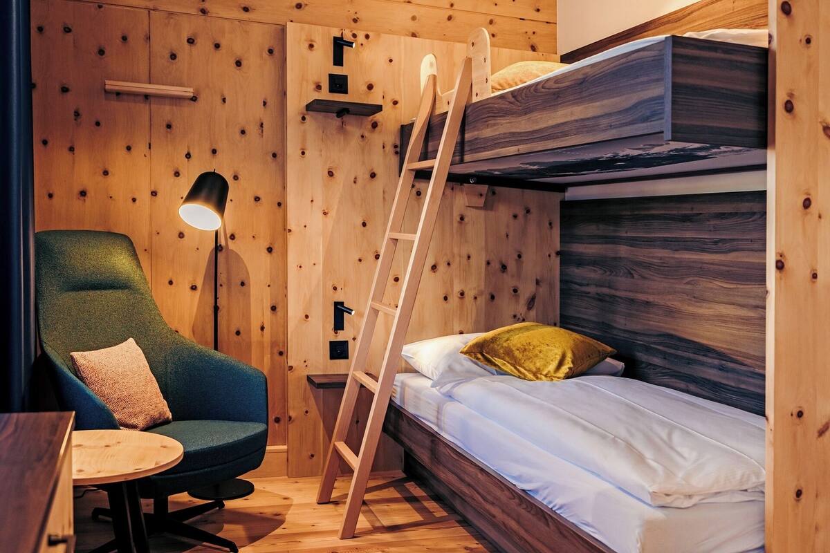 A compact room with a bunk bed, a desk, a chair, and a ladder.
