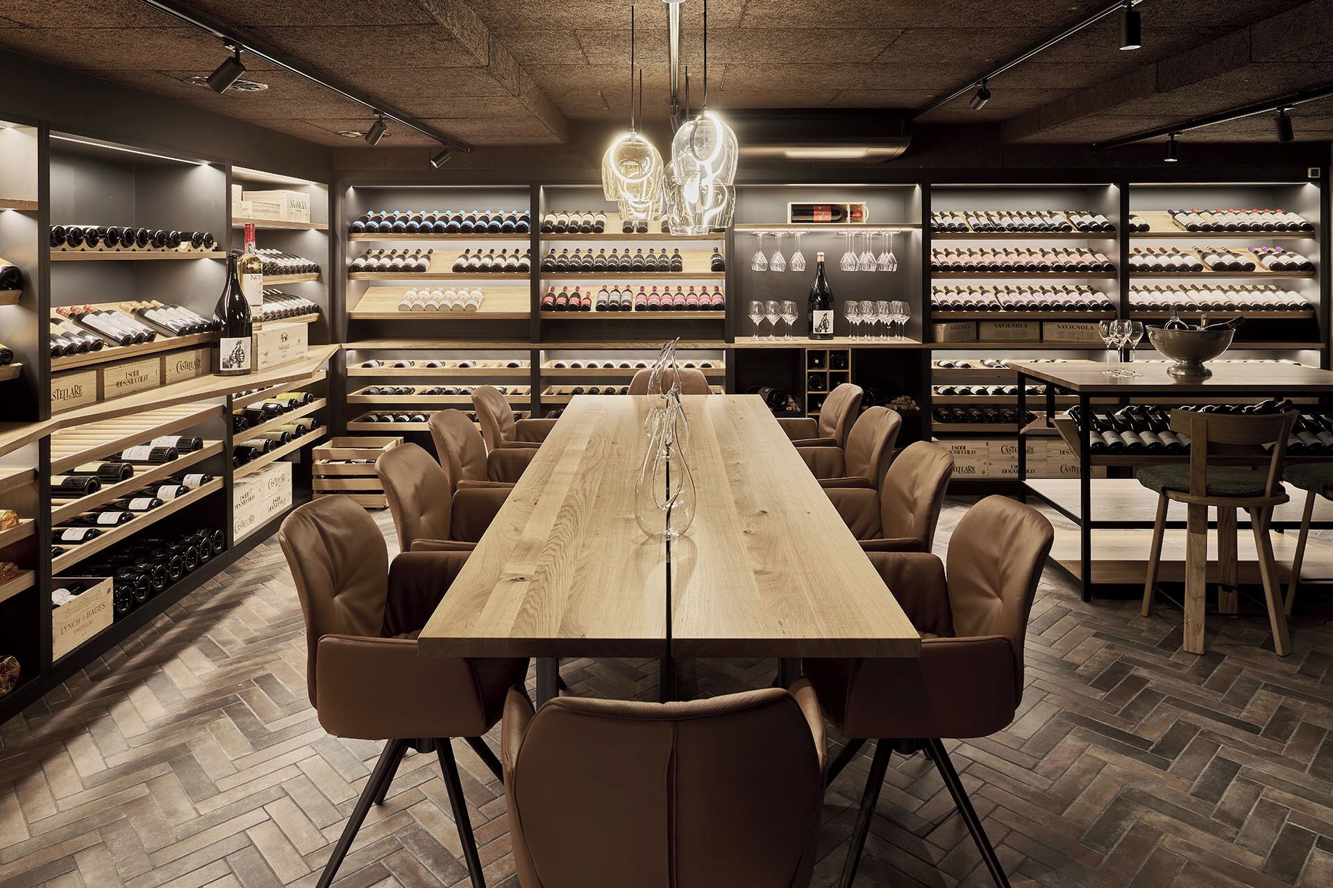 A wine cellar with a long wooden table and leather chairs, surrounded by shelves of wine bottles and glasses.