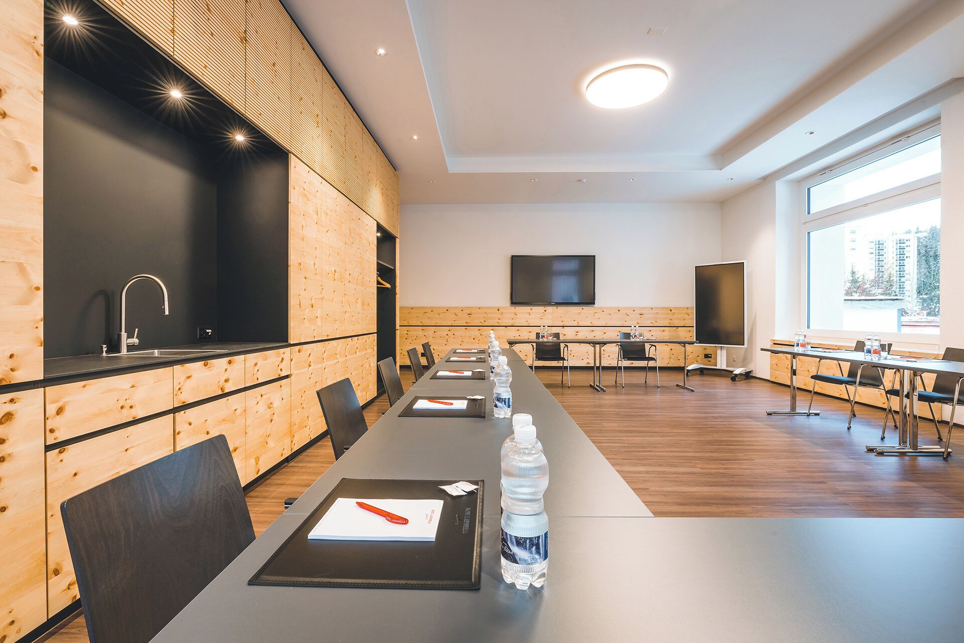A conference room with a long table, chairs, a sink, and a large window.