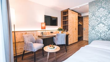 Una habitación de hotel con una cama, dos sillones, una mesita con fruta, un escritorio con lámpara, un televisor y un armario.