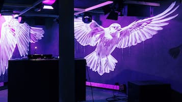 Une pièce dotée d’un grand écran sur lequel est projeté un oiseau en vol, d’une table de mixage pour DJ et d’un haut-parleur.