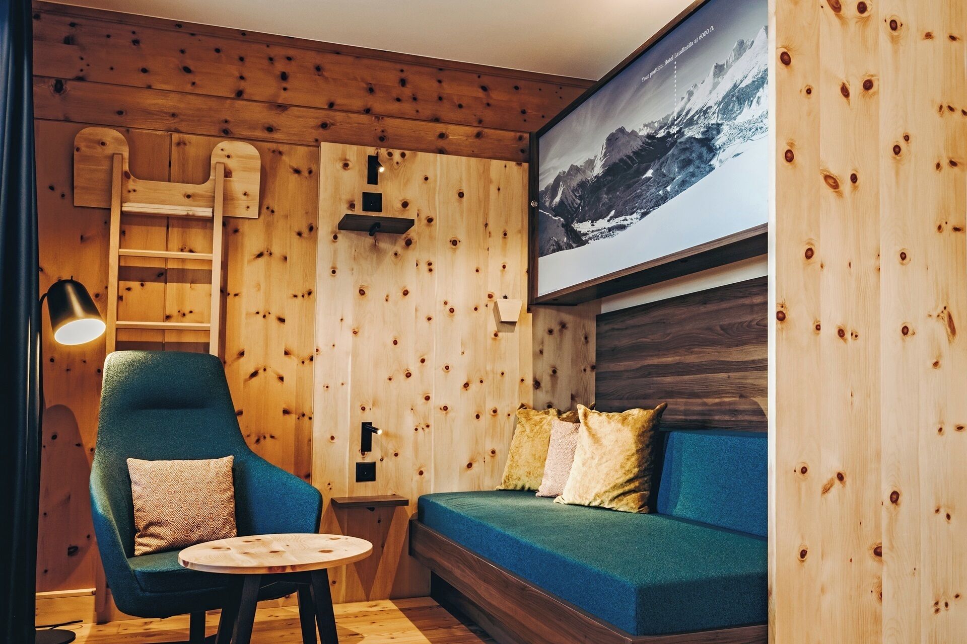 Um quarto acolhedor com parede de madeira, um sofá azul, uma poltrona verde e uma pequena mesa redonda.