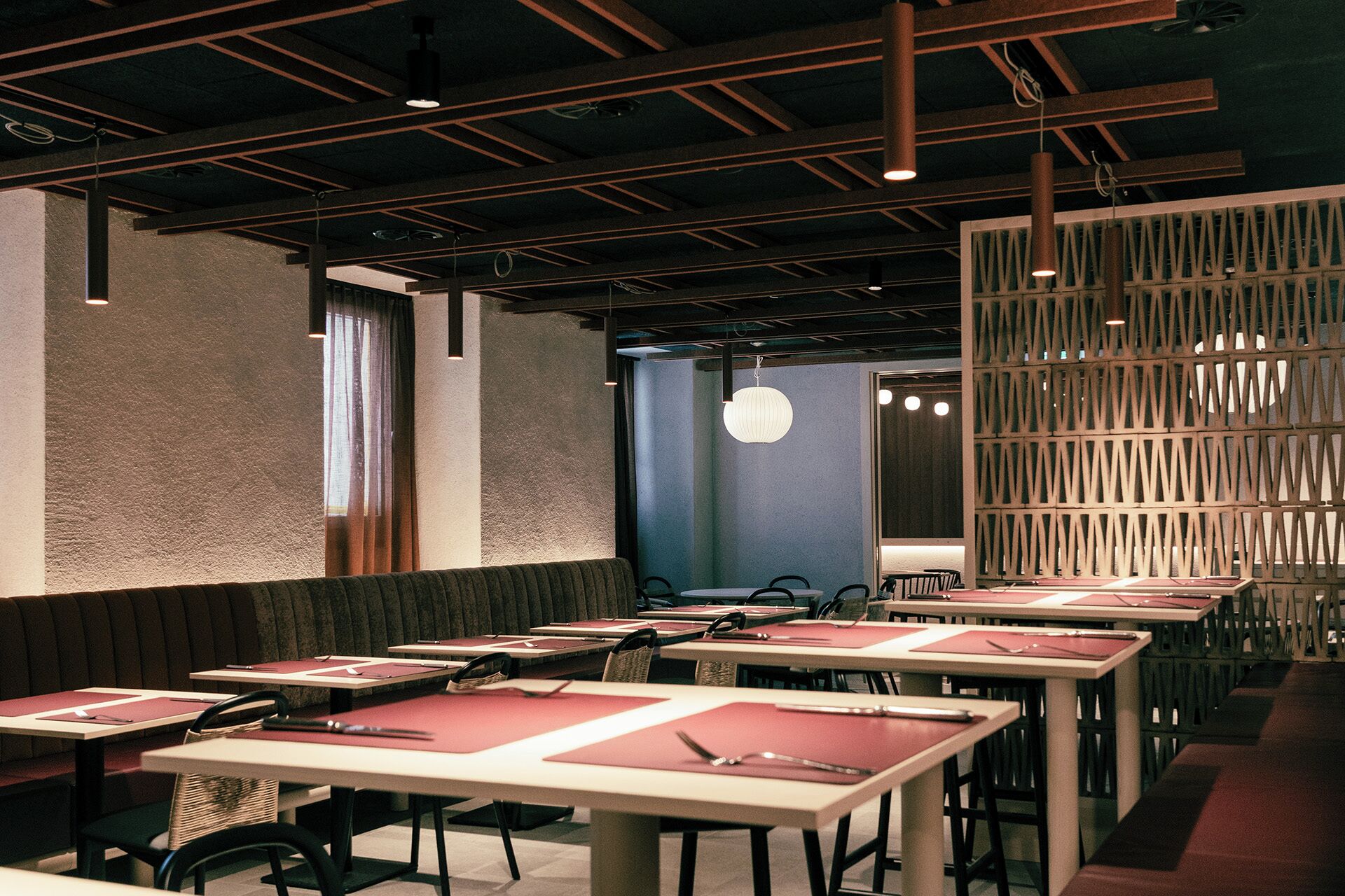 A restaurant with booths and tables, a patterned wall, and pendant lighting.