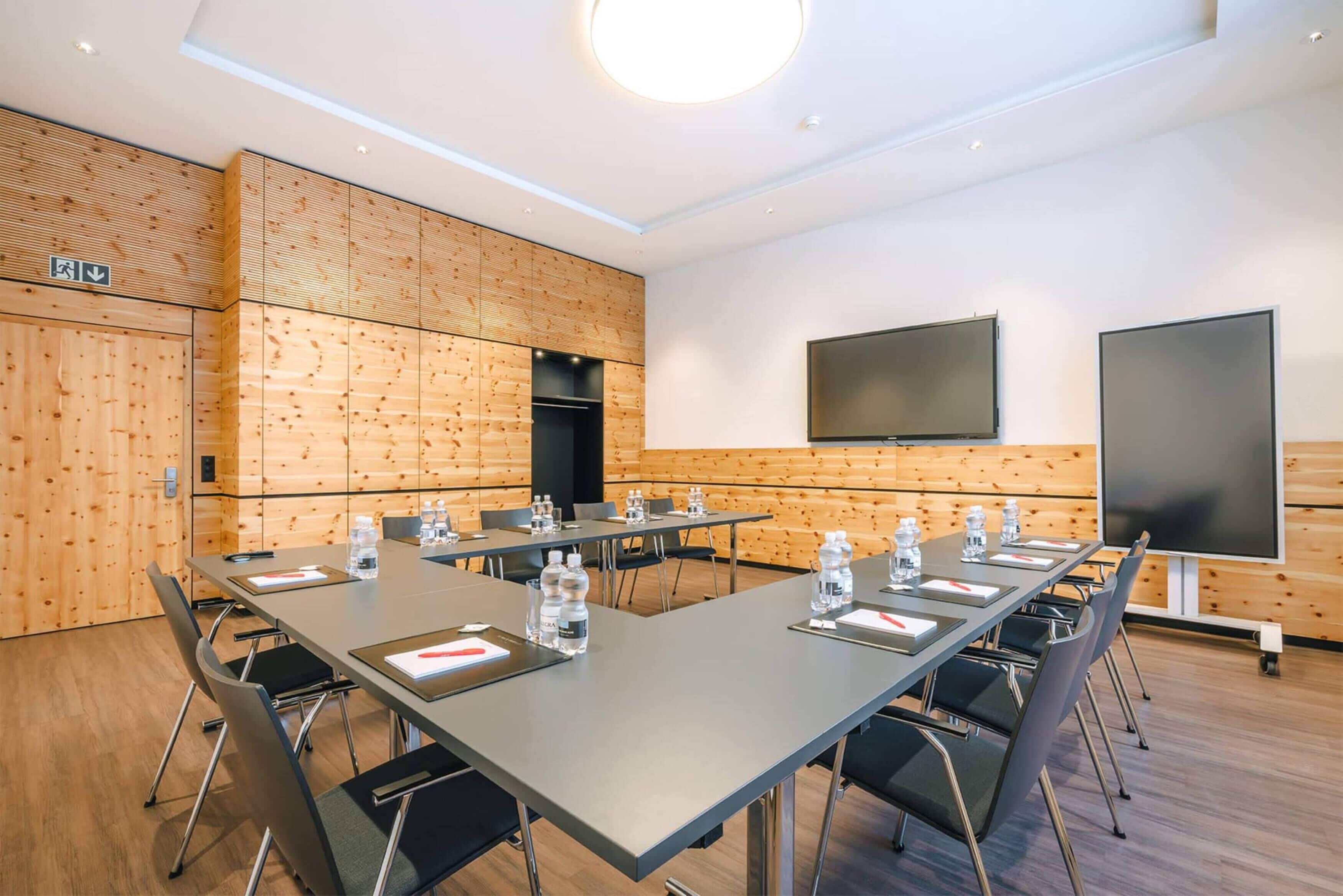 A conference room with long tables, chairs, and a large screen.