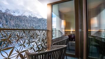 Varanda com vista para montanhas cobertas de neve, cadeiras de vime e porta de vidro que dá para um quarto com abajur.