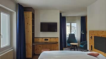 Habitación de hotel con cama, escritorio, televisor, una silla y vistas al exterior.