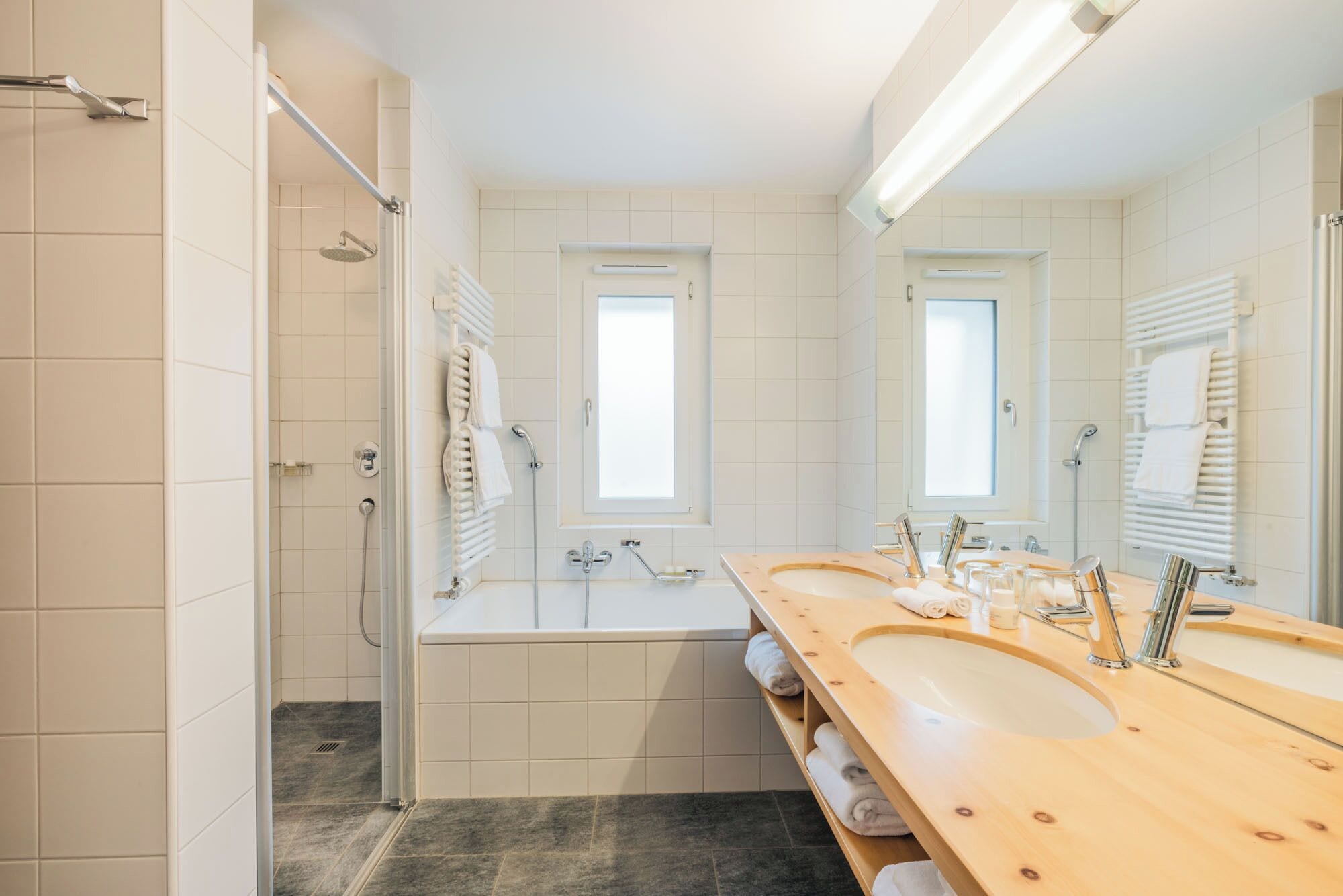 Une salle de bain moderne avec une baignoire, deux lavabos, une douche et un grand miroir.