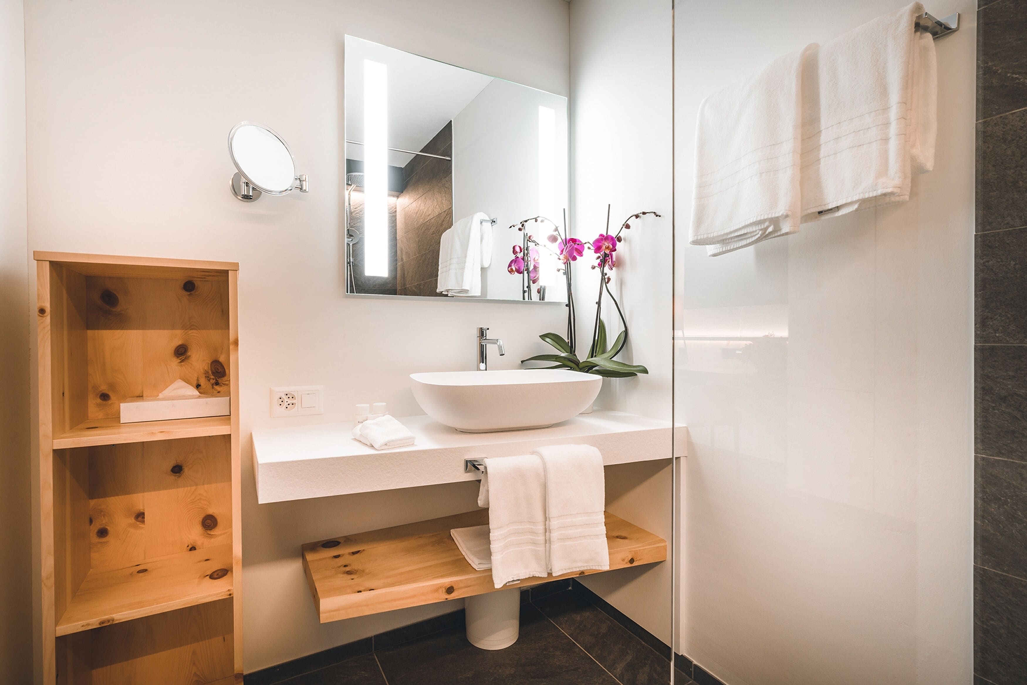 Un baño moderno con tocador de madera, lavamanos blanco y un espejo grande.