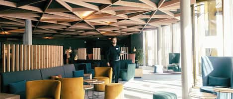 Un interior moderno con diseño geométrico en el techo, asientos cómodos y ventanas amplias que dejan entrar luz natural.