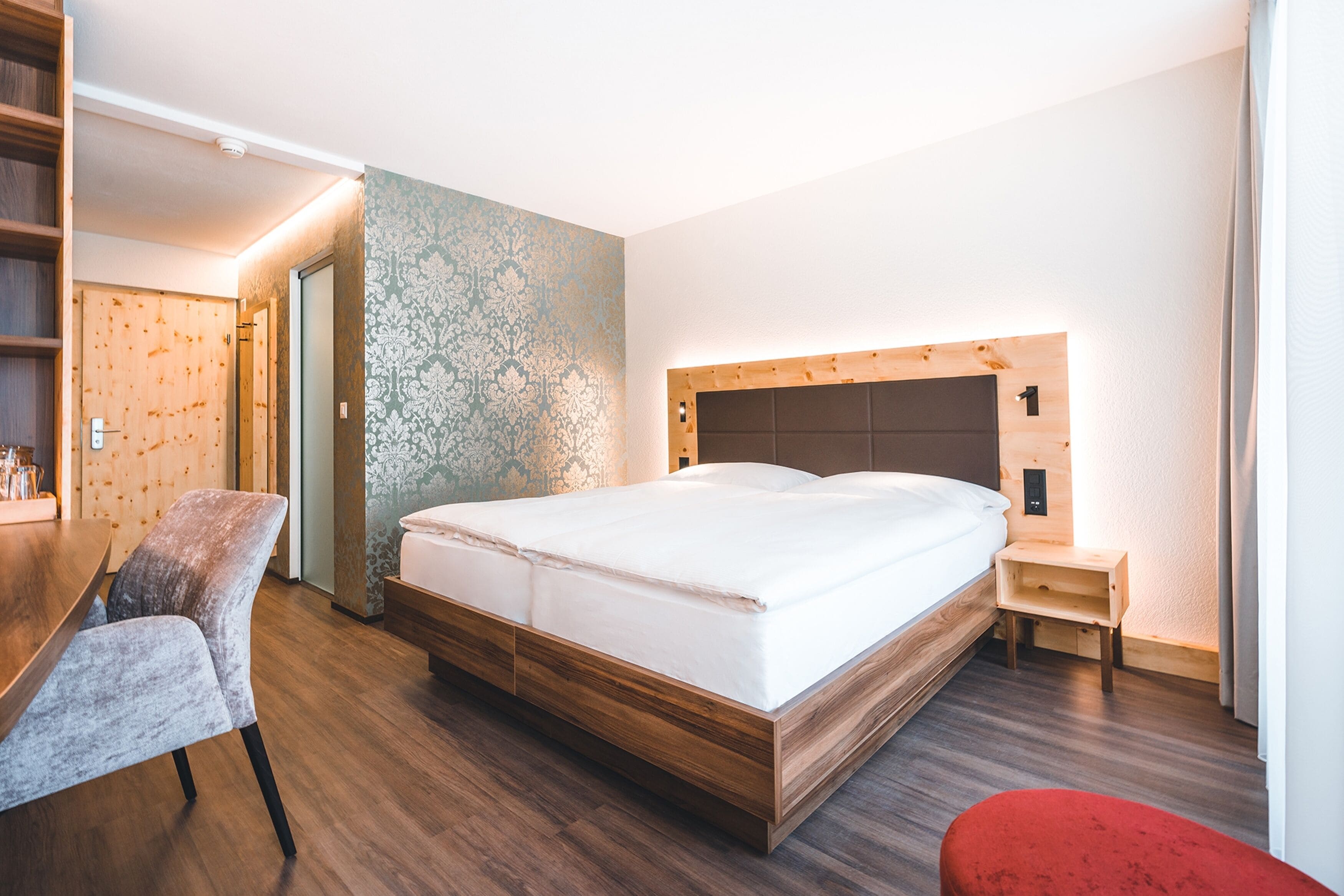 Una habitación de hotel moderna con una cama de madera, un escritorio pequeño y una silla roja.
