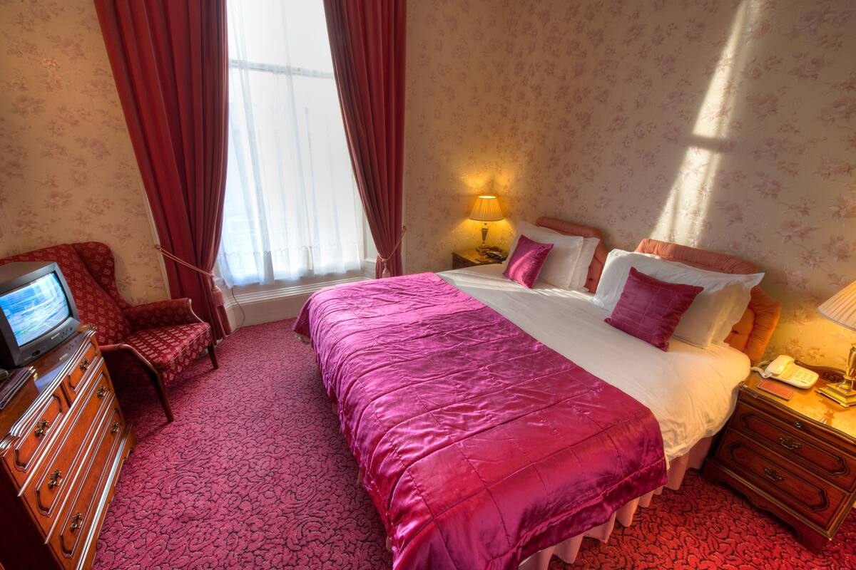 A hotel room with a large bed, a TV, a dresser, and a window with curtains.