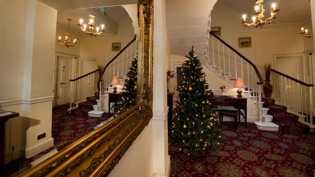 Eine prächtige Treppe mit Weihnachtsbaum, kunstvollen Chandeliers und einem großen Spiegel, der den Raum widerspiegelt.