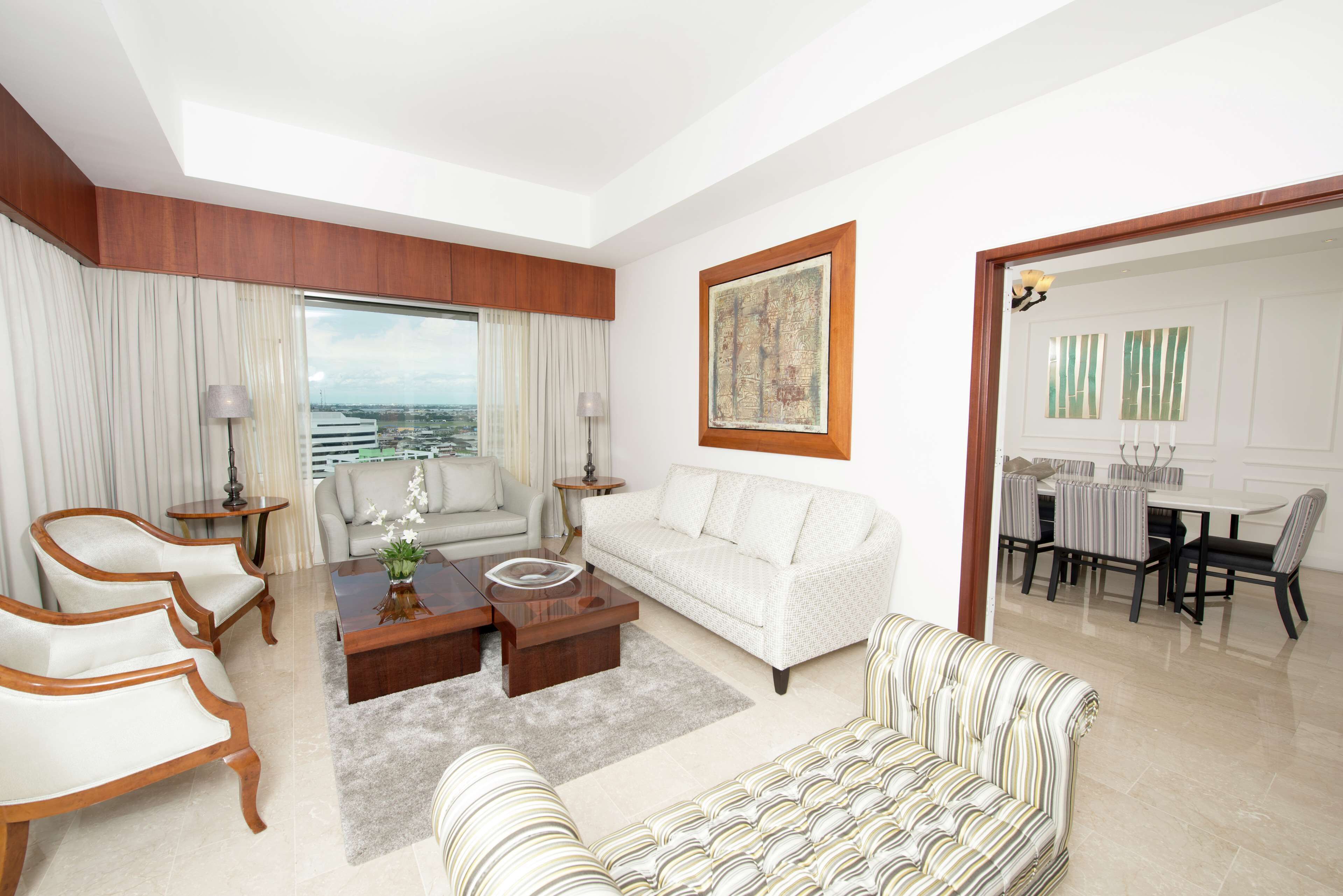 A modern living room with a sofa, armchairs, a coffee table, and a dining area with a table and chairs.