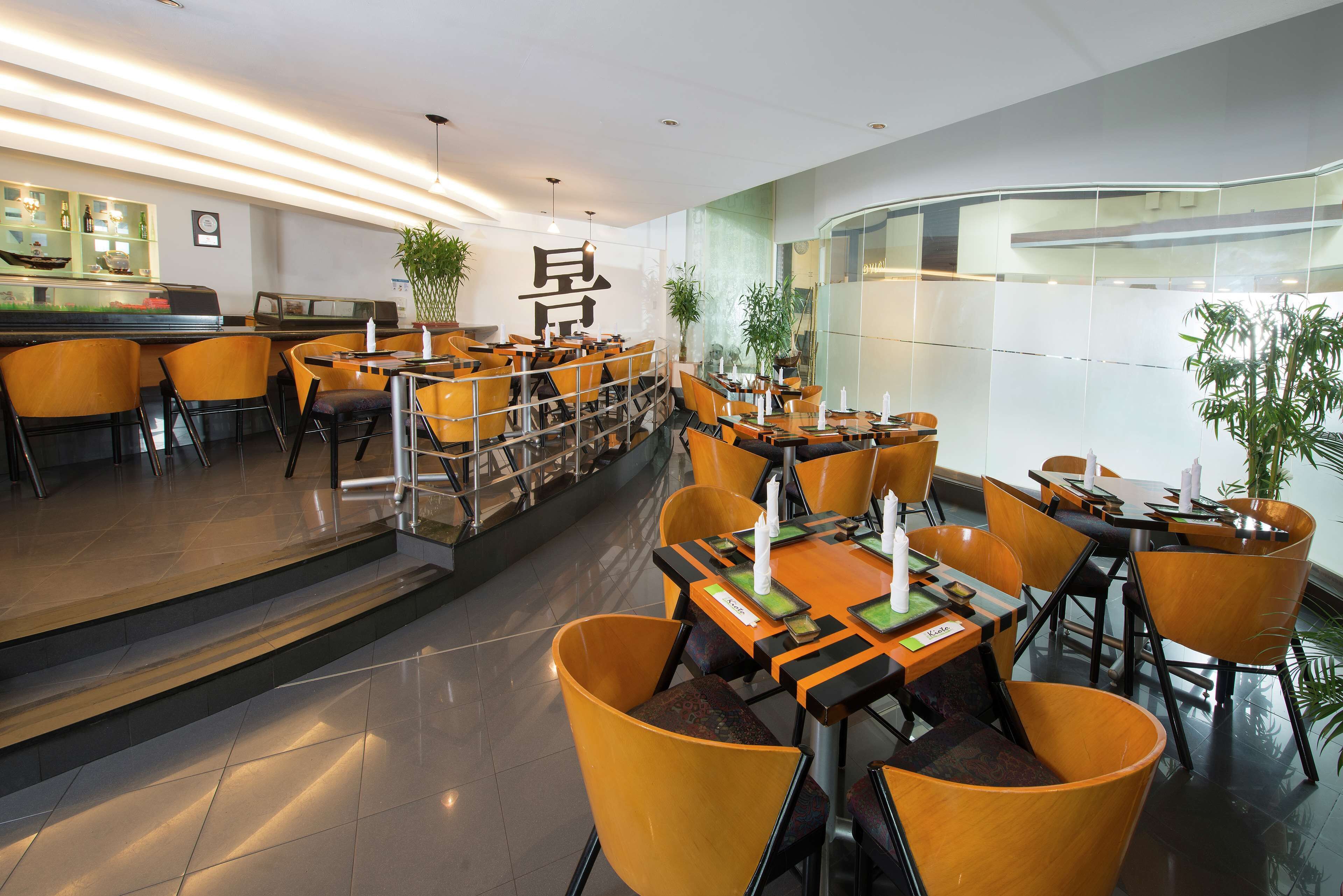 A modern restaurant with yellow chairs and tables, a bar area, and large windows.