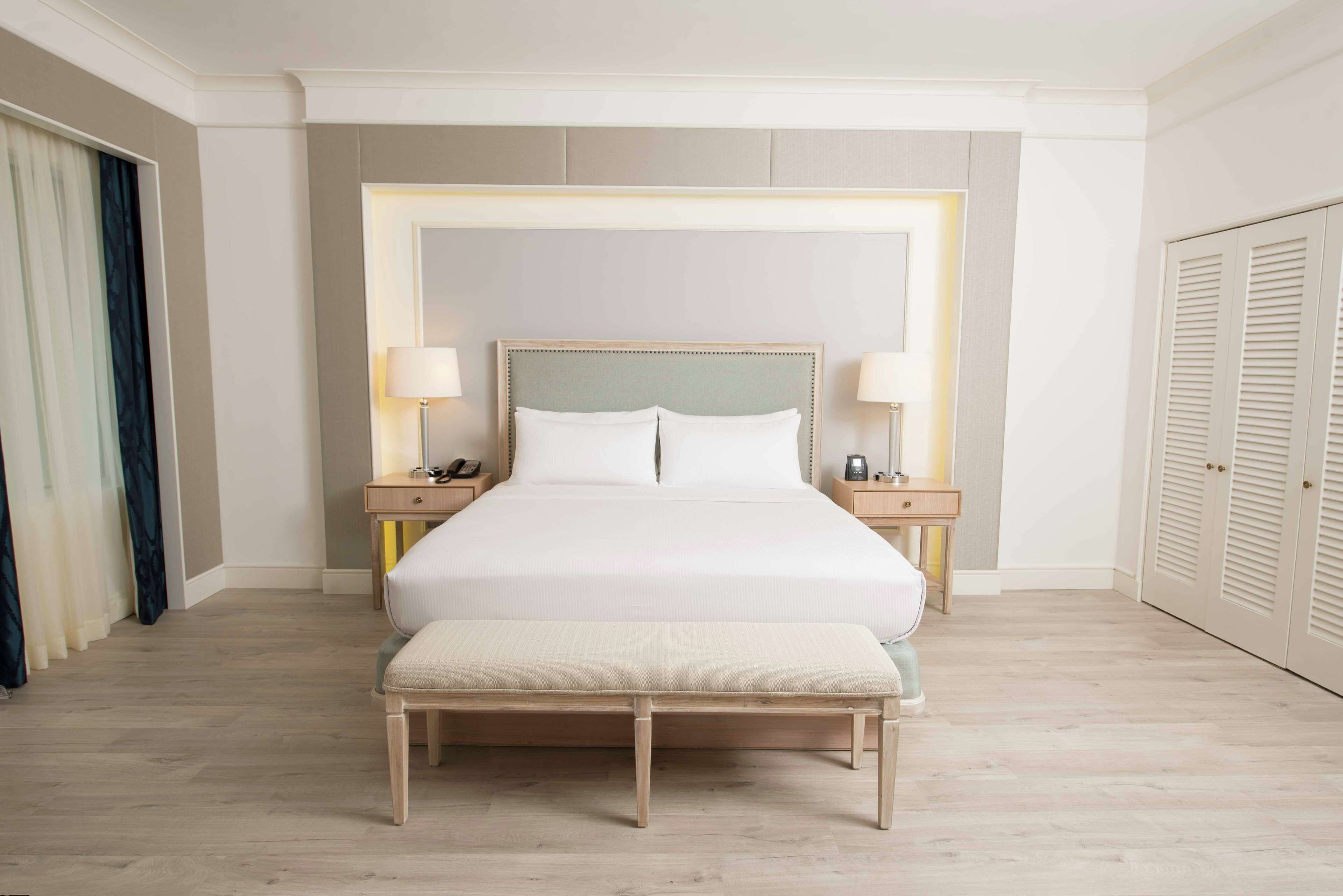 A neatly arranged hotel room with a large bed, bedside tables, a bench, and a wardrobe.