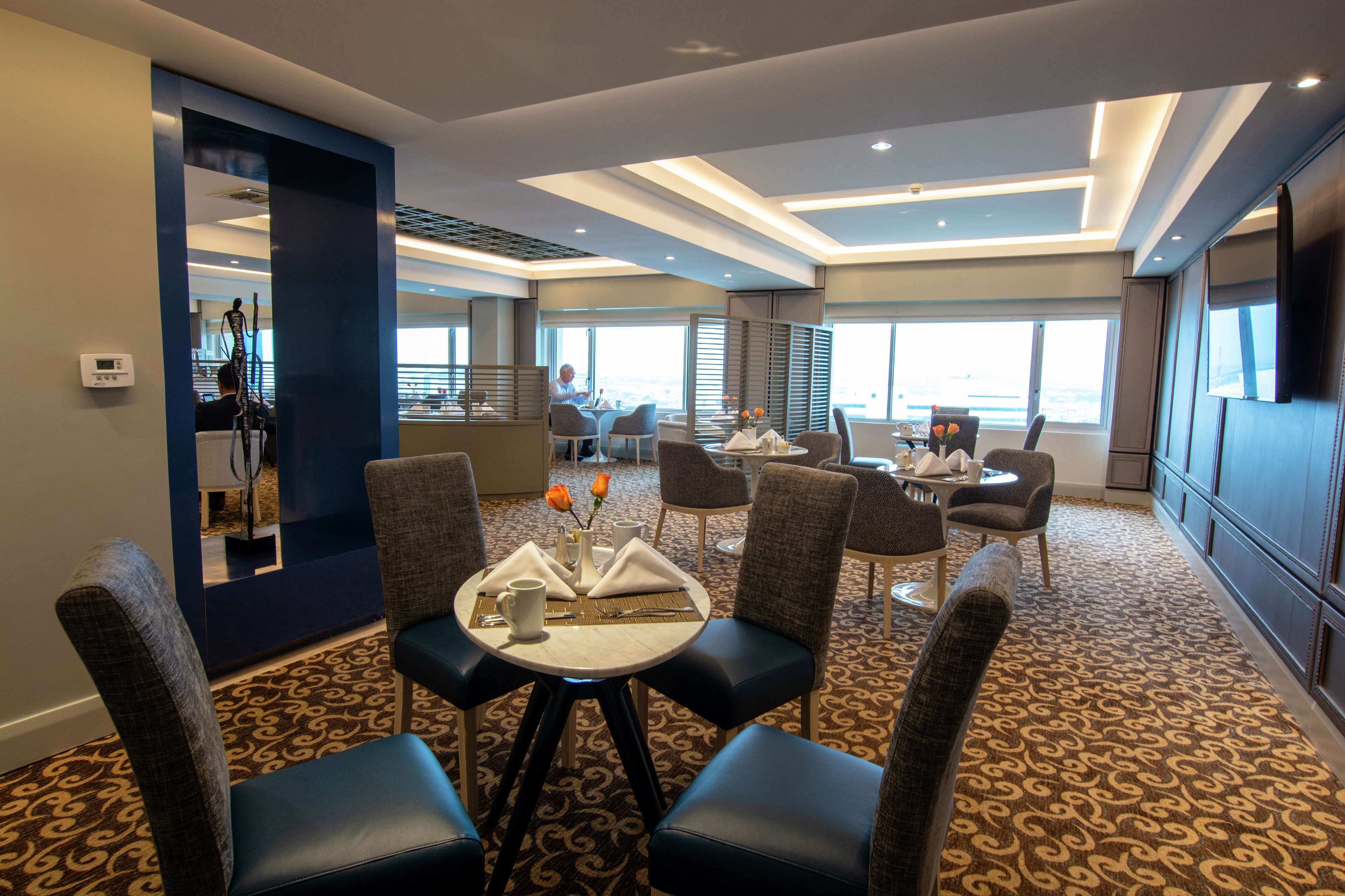 A hotel dining area with round tables, chairs, and a view of the city.