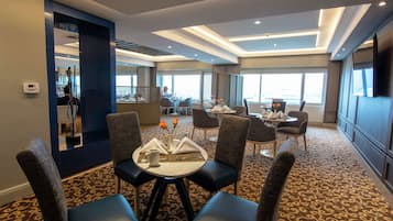 A hotel dining area with round tables, chairs, and a view of the city.