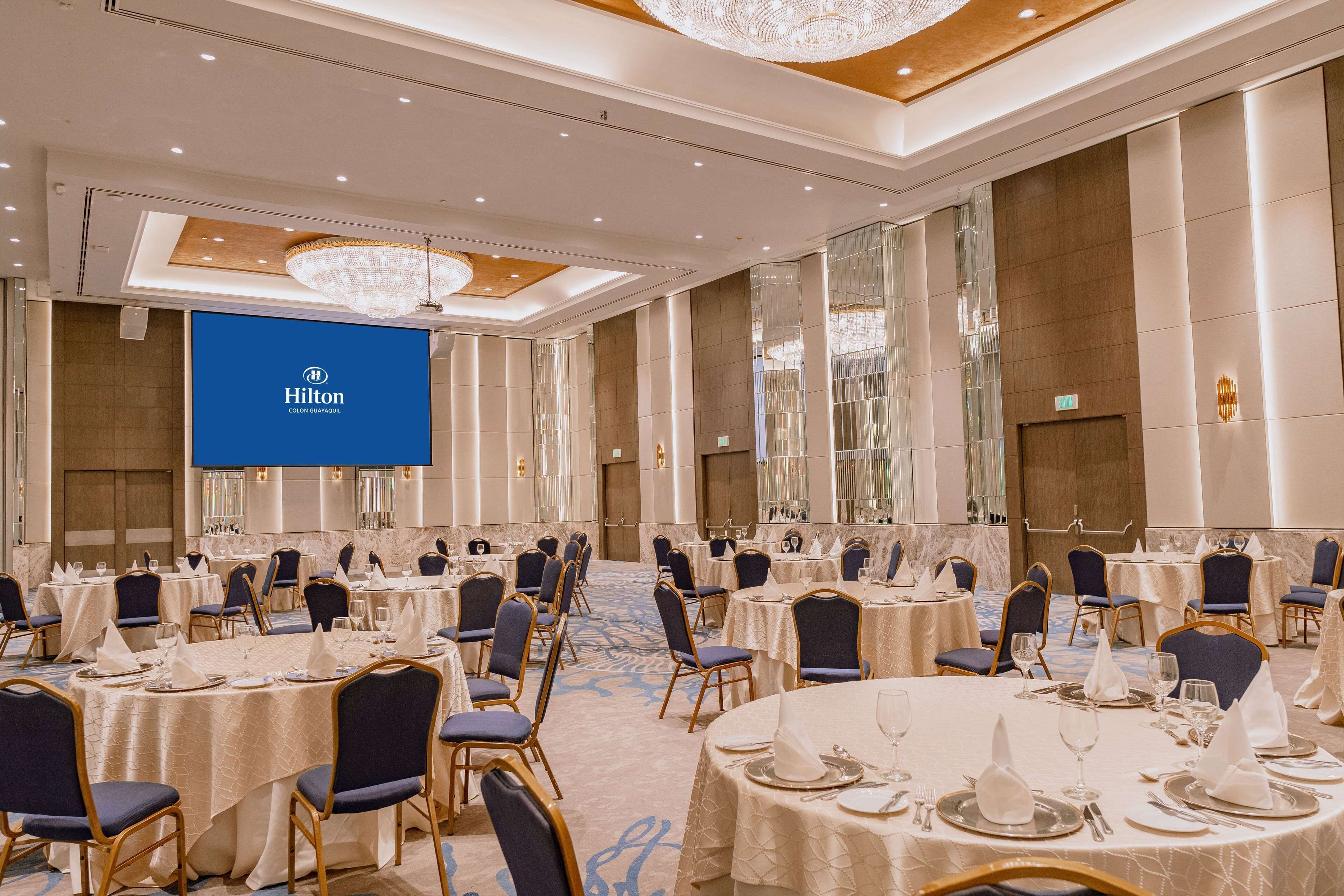 Un salón de eventos de Hilton con varias mesas redondas dispuestas para cenar, organizadas en filas con sillas azules.