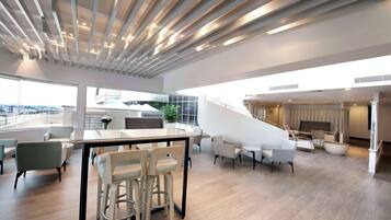 A spacious, modern living area with a high ceiling, a staircase, and a view of the city.