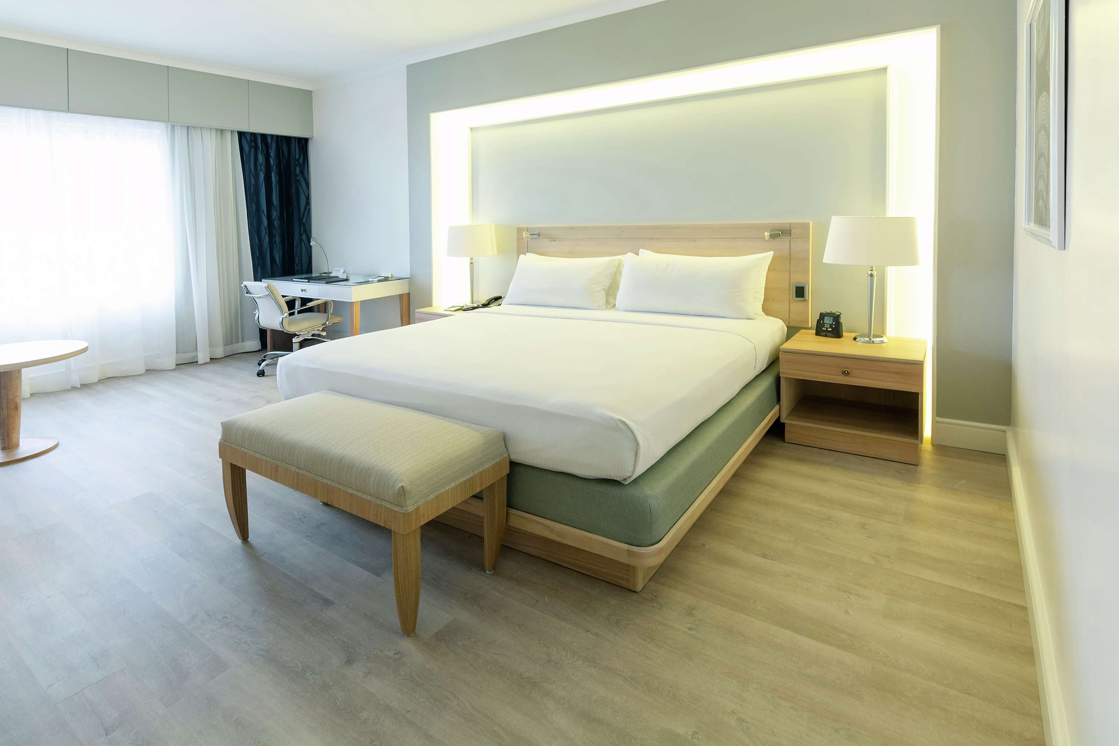 A modern hotel room with a large bed, bedside tables, a desk, and a chair.