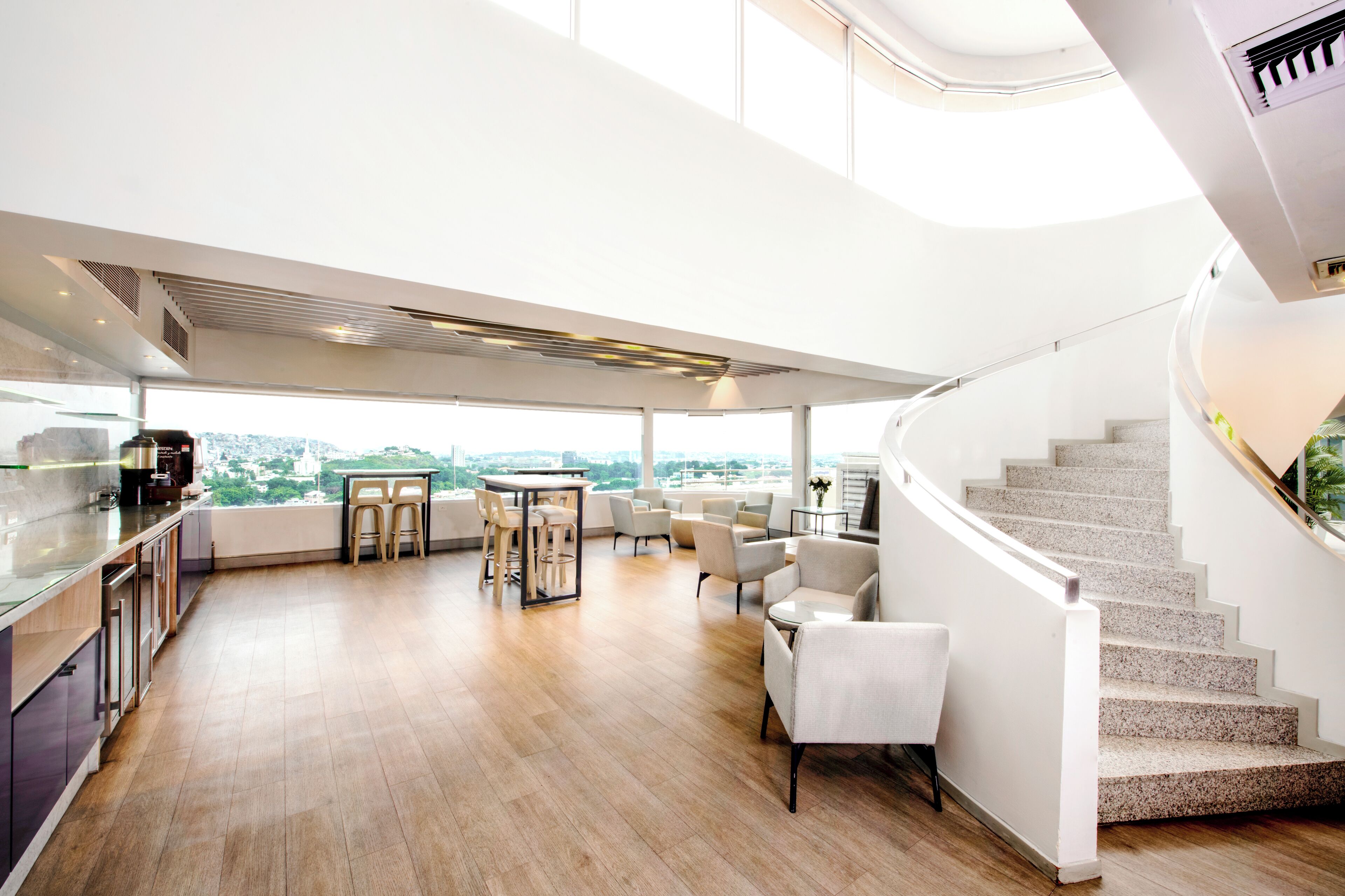 A spacious living area with a kitchen, dining table, and seating. A staircase leads to an upper level.