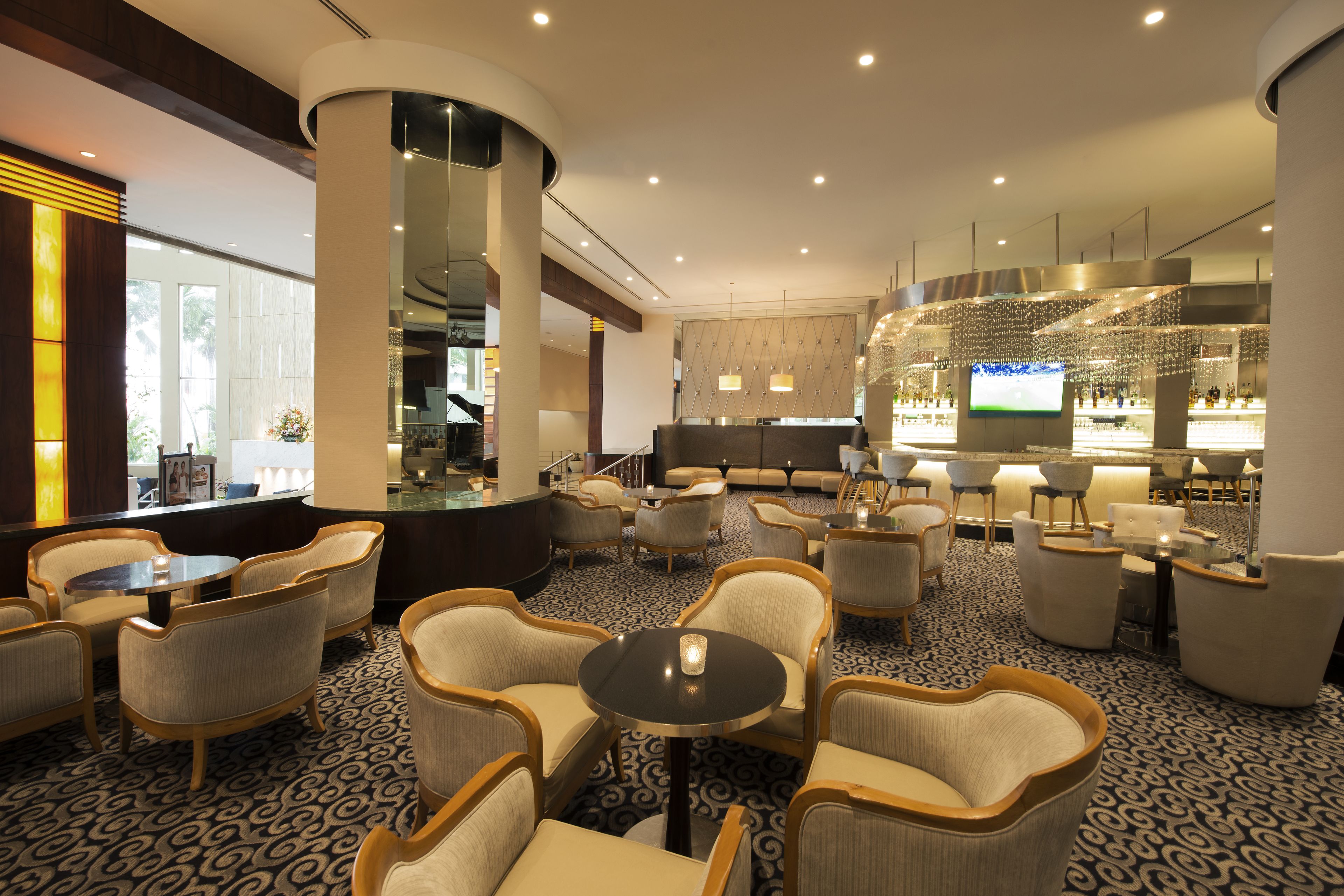 A hotel lobby with a bar area, seating arrangements, and a large screen displaying a sports event.