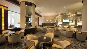 A hotel lobby with a bar area, seating arrangements, and a large screen displaying a sports event.