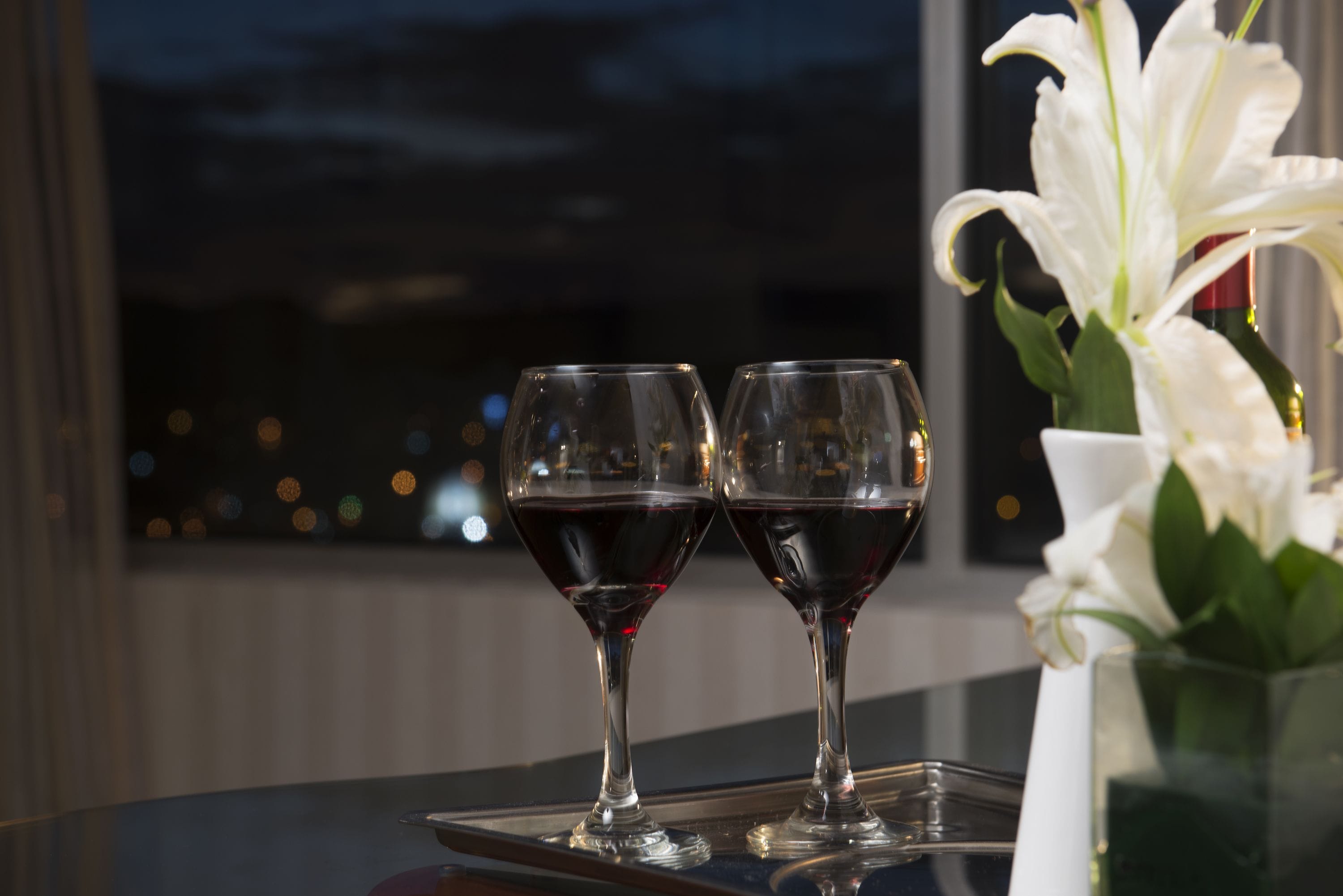 Two wine glasses on a tray with a white flower vase.