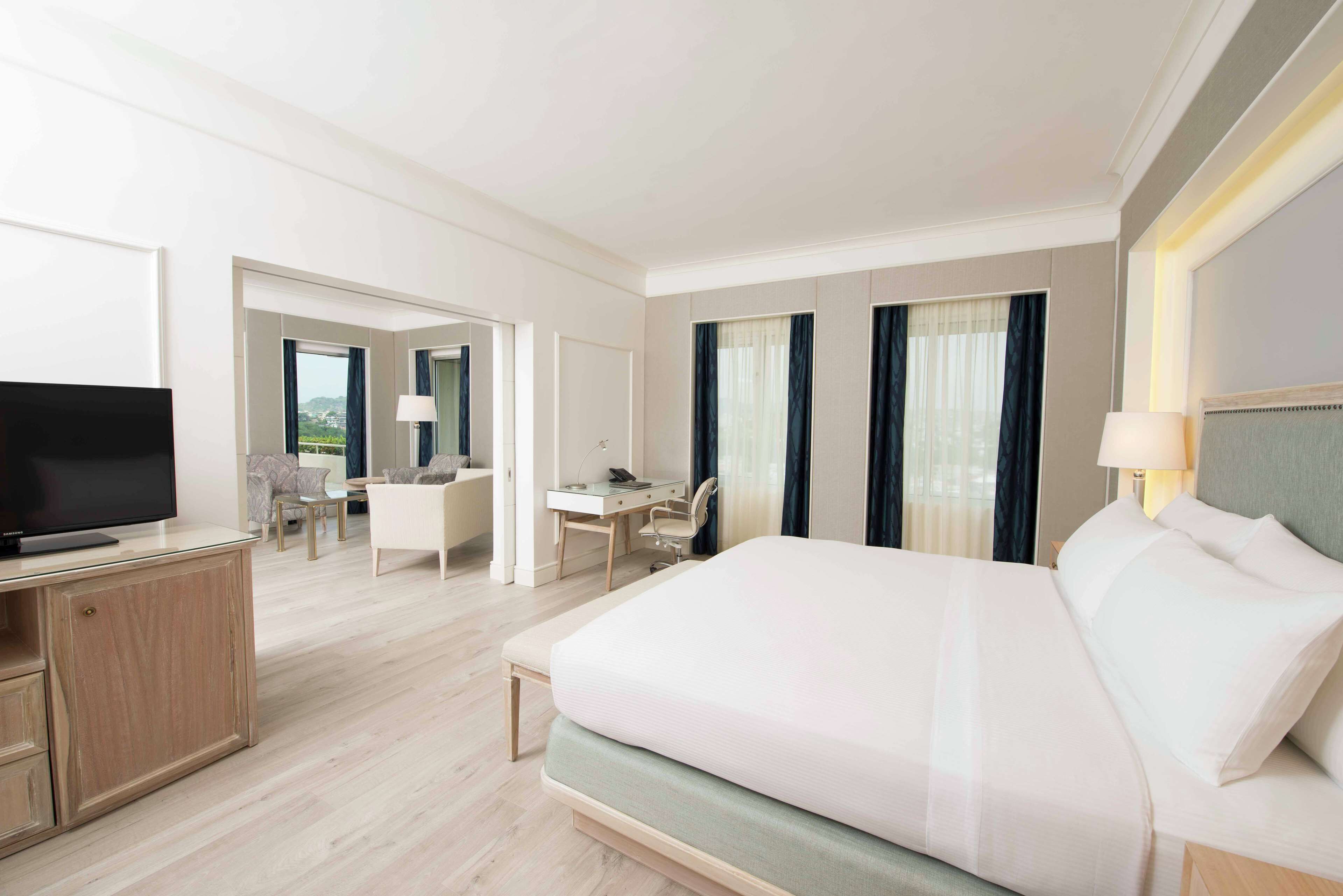 Habitación de hotel con una cama grande, un escritorio, una silla, un televisor y vistas al exterior.