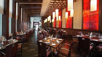 A spacious restaurant with long tables and chairs, warm lighting, and a modern interior design.
