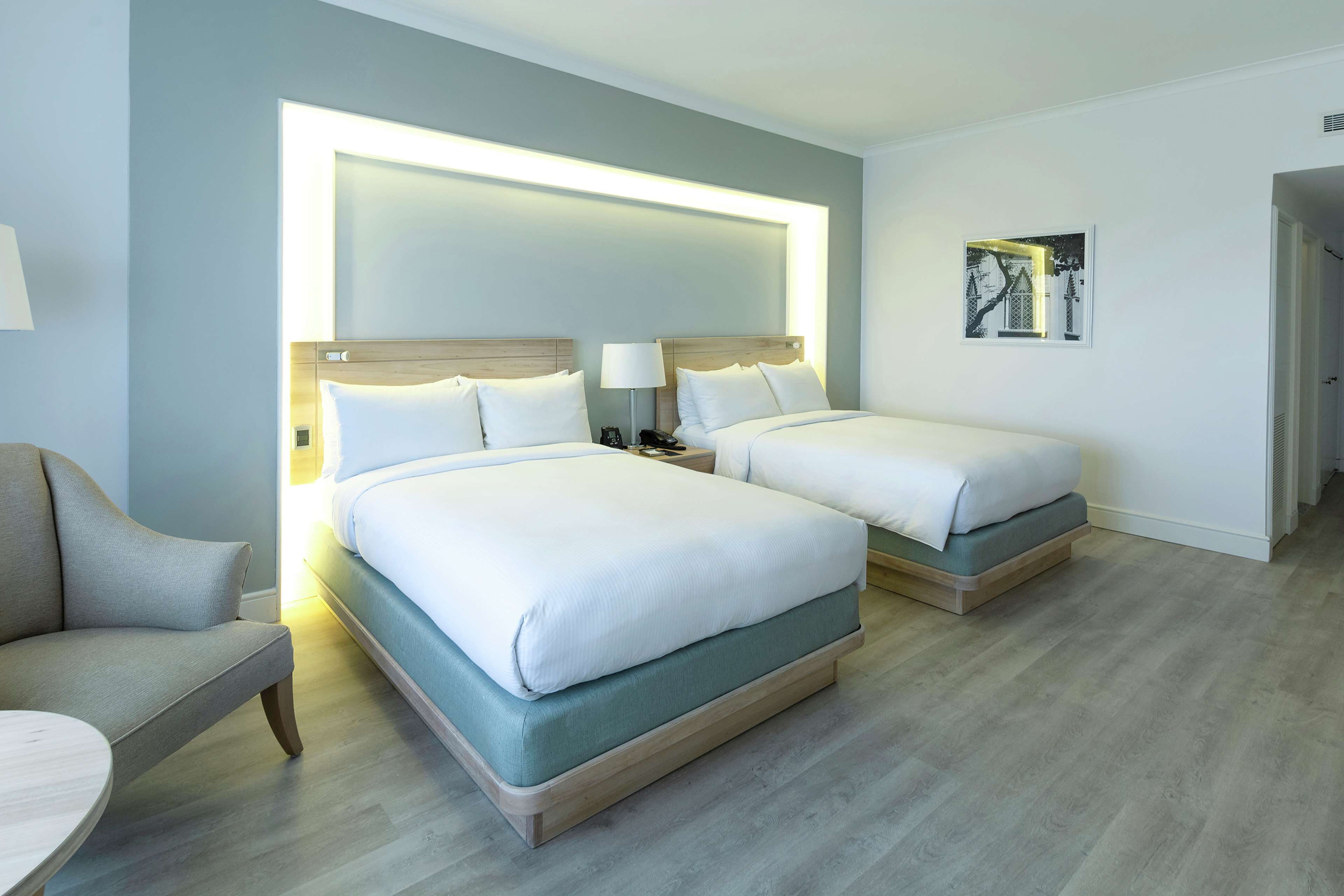A hotel room with two beds, a sofa, a bedside table, and a lamp.