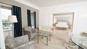 Une chambre d’hôtel comprenant un canapé, des fauteuils, une table basse en verre, un lit et une table à manger avec des chaises.