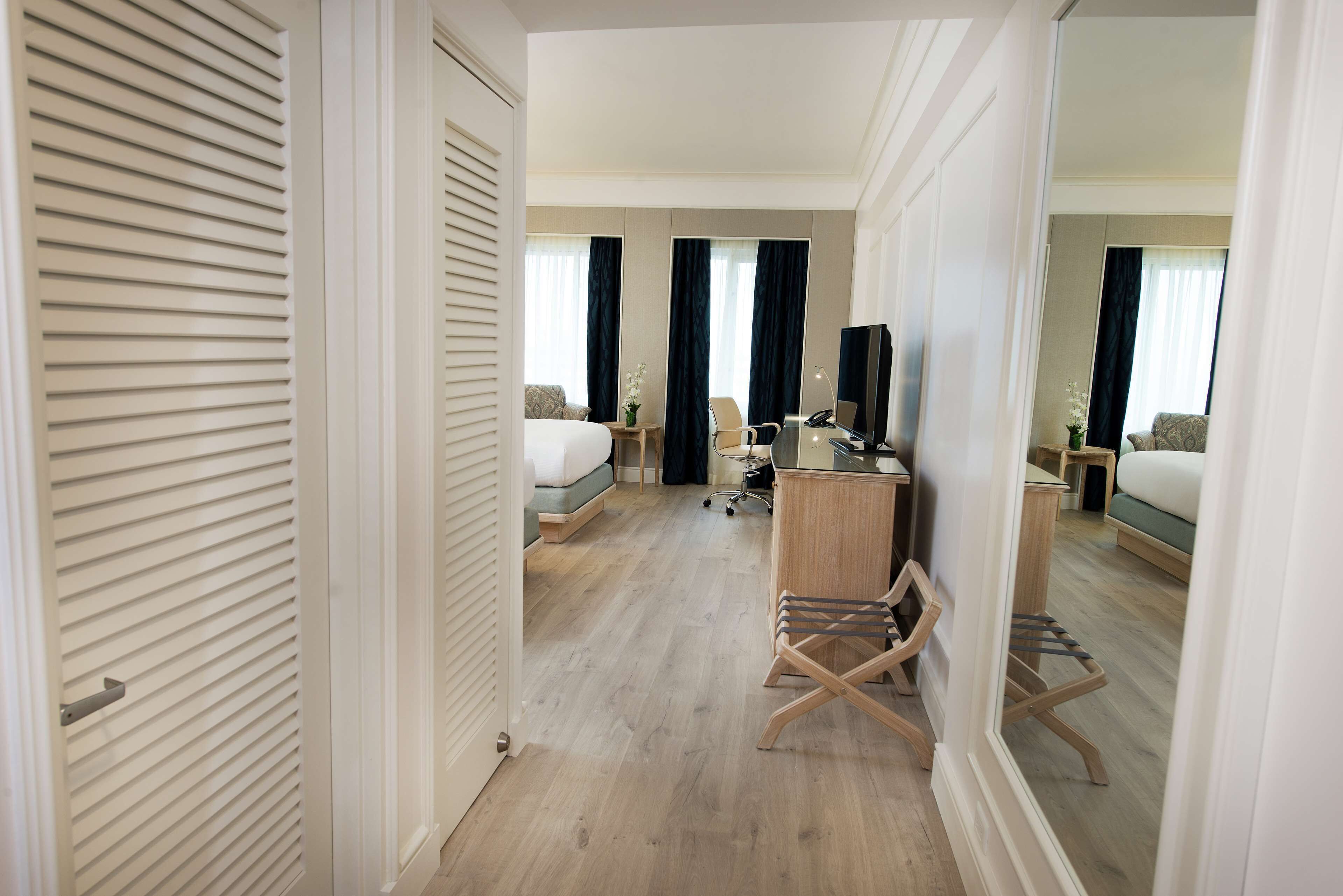 A hotel room with a bed, desk, chair, and a mirror.