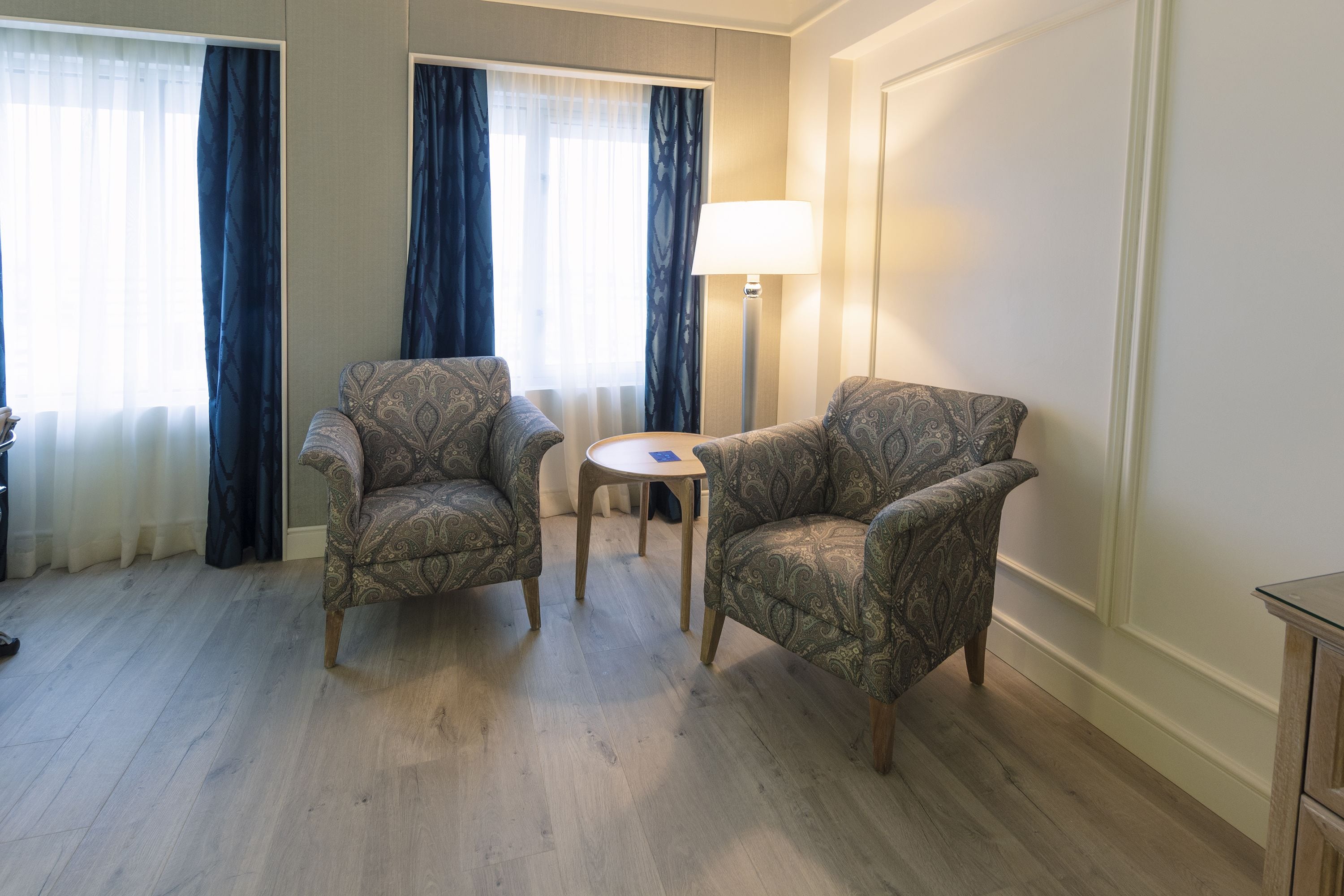 Una habitación con dos sillones estampados, una mesita redonda pequeña y una lámpara de pie.