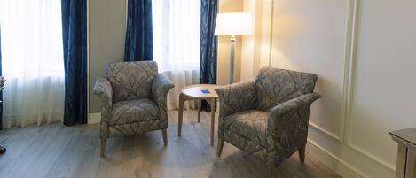 A room with two patterned armchairs, a small round table, and a floor lamp.