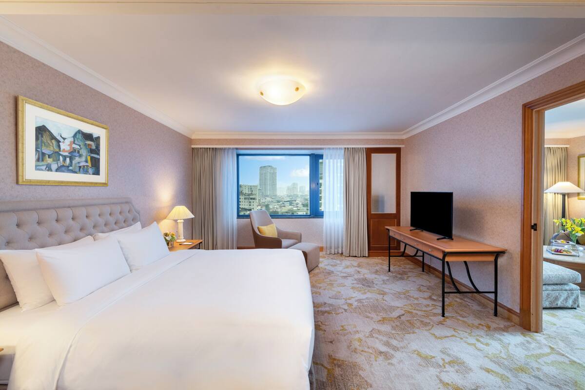 A hotel room with a large bed, a television, a desk, and a window with a city view.