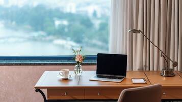 A desk with a laptop, a cup of coffee, a vase with a flower, and a lamp.