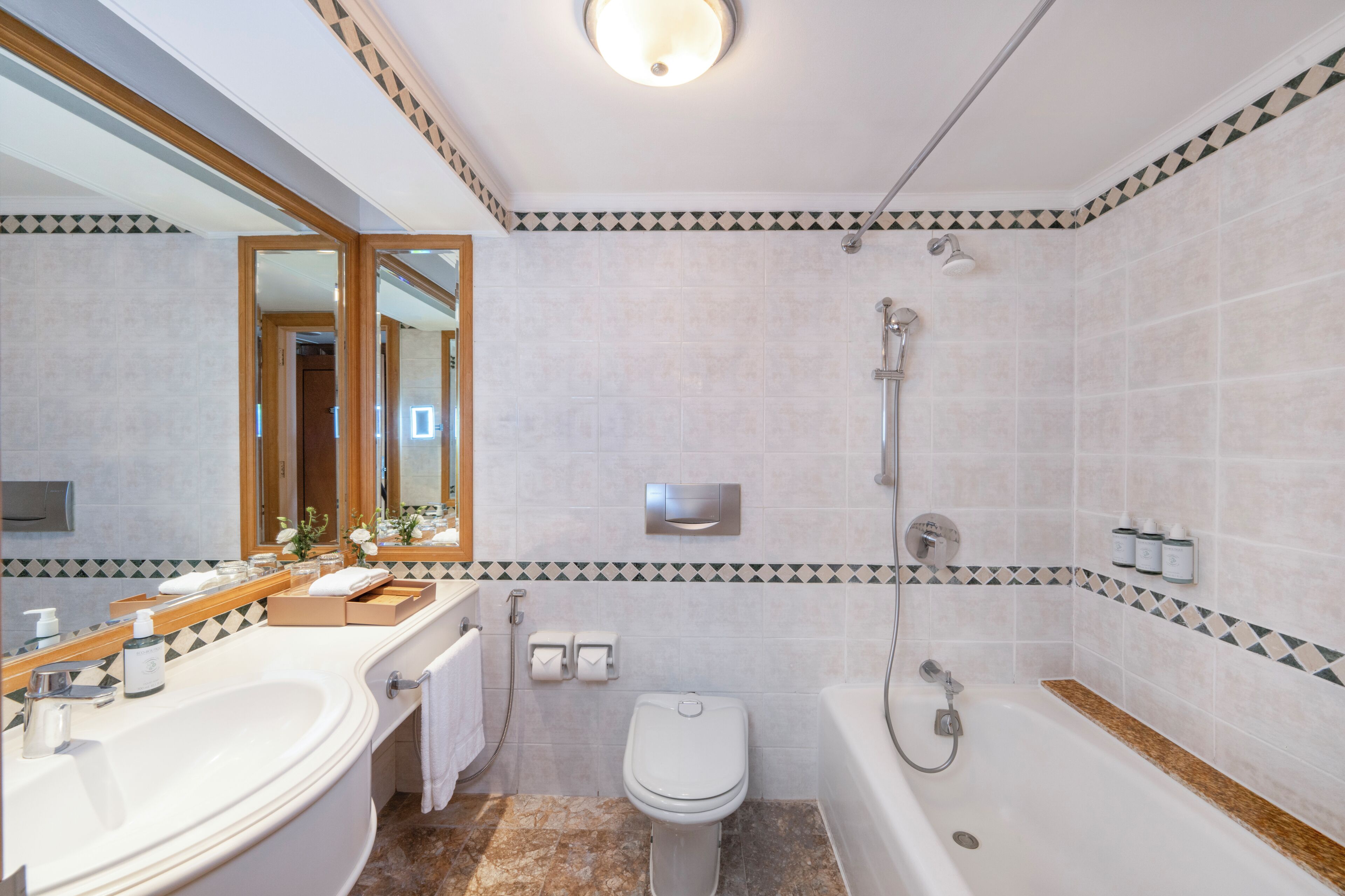 A bathroom with a bathtub, toilet, and sink, featuring a tiled wall with a geometric pattern and a mirror above the sink.
