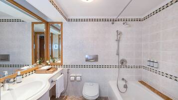 A bathroom with a bathtub, toilet, and sink, featuring a tiled wall with a geometric pattern and a mirror above the sink.