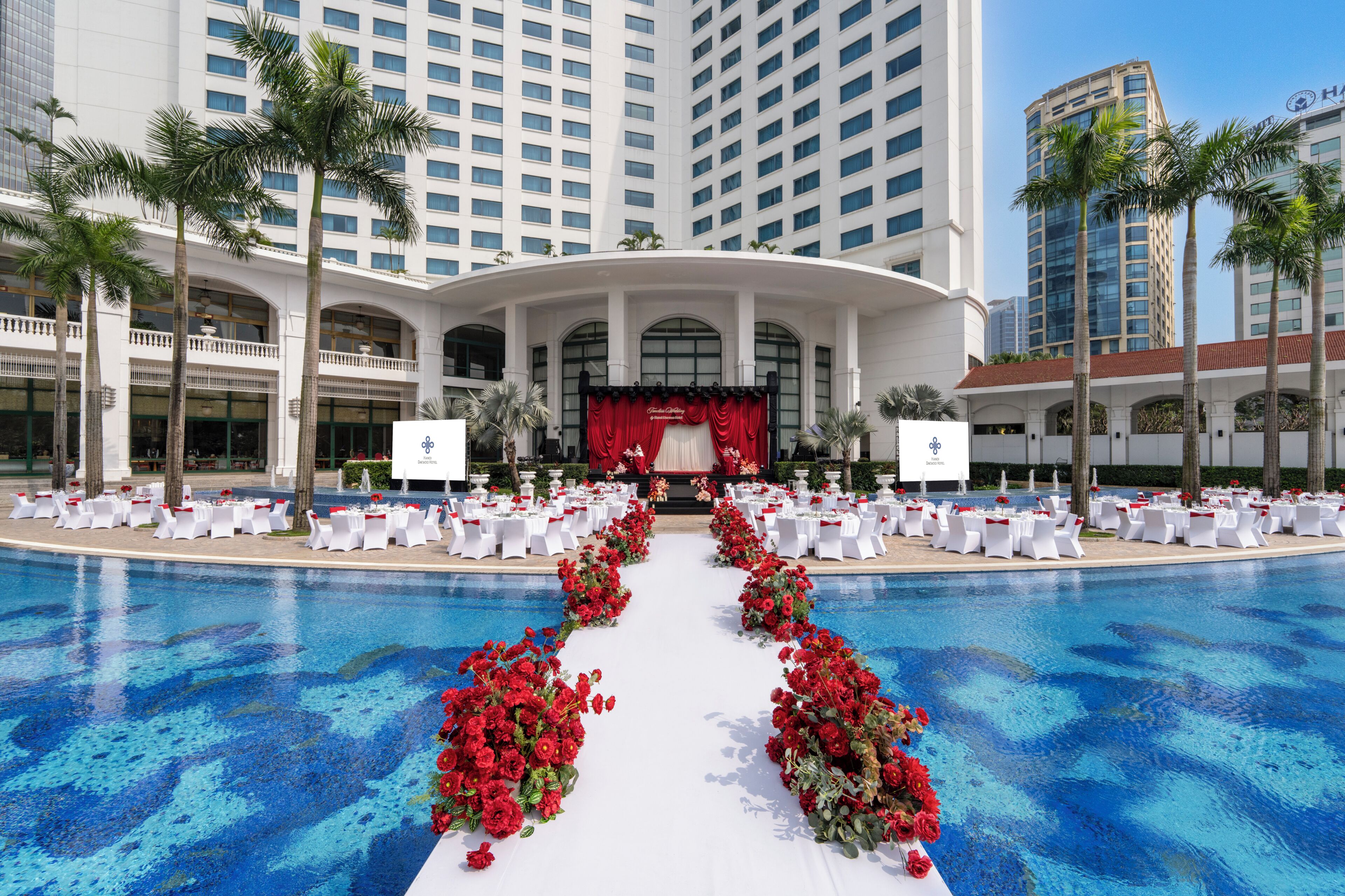 A hotel with a pool, white tables, and chairs arranged for an event.