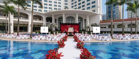 A hotel with a pool, white tables, and chairs arranged for an event.