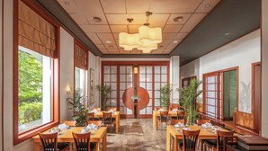 Un restaurante con mesas y sillas de madera, ventanas amplias y un elemento decorativo central.