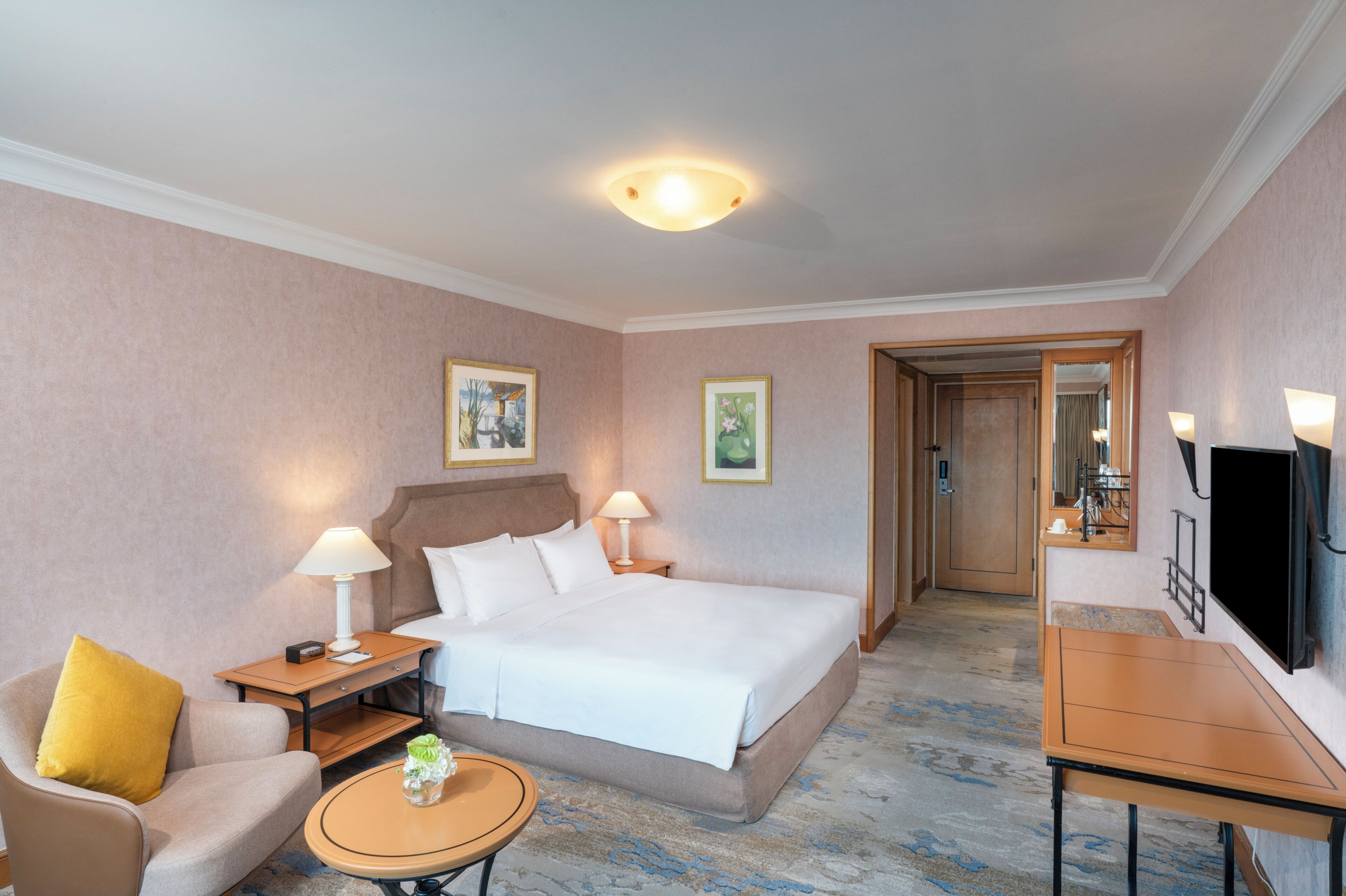 A hotel room with a bed, a sofa, a small table, a TV, and a mirror.