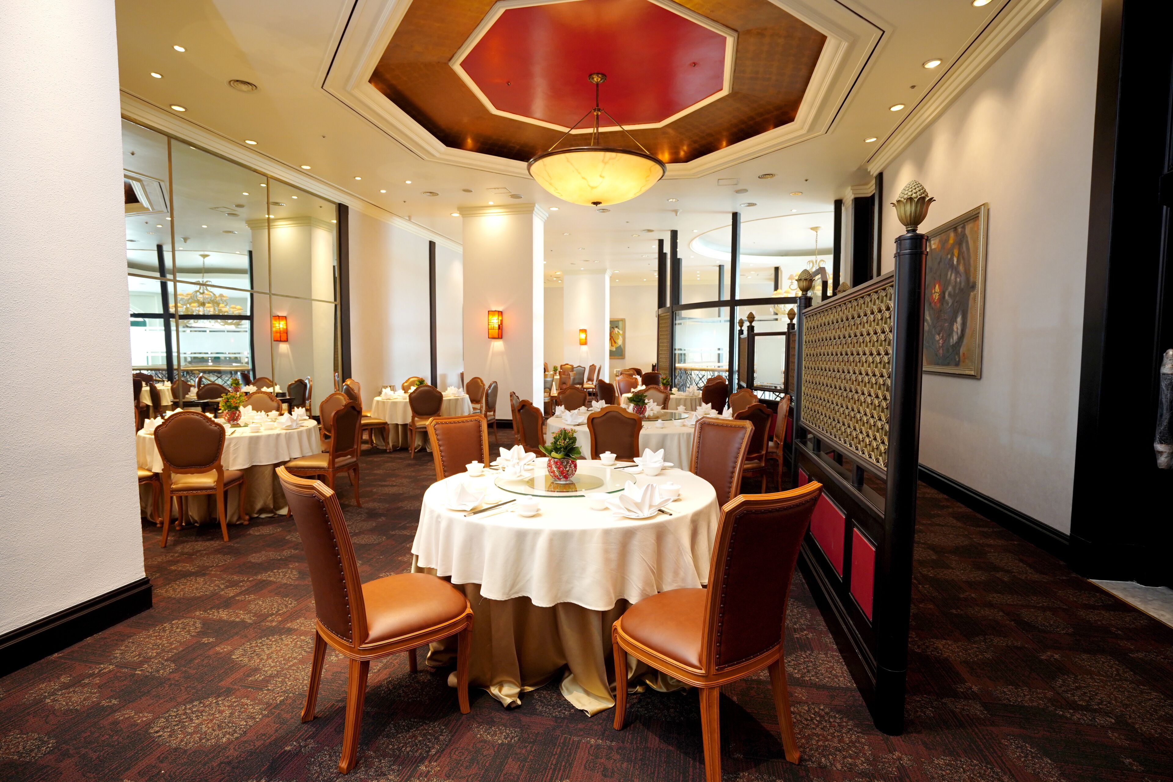 A dining area with round tables, brown leather chairs, and a red ceiling.