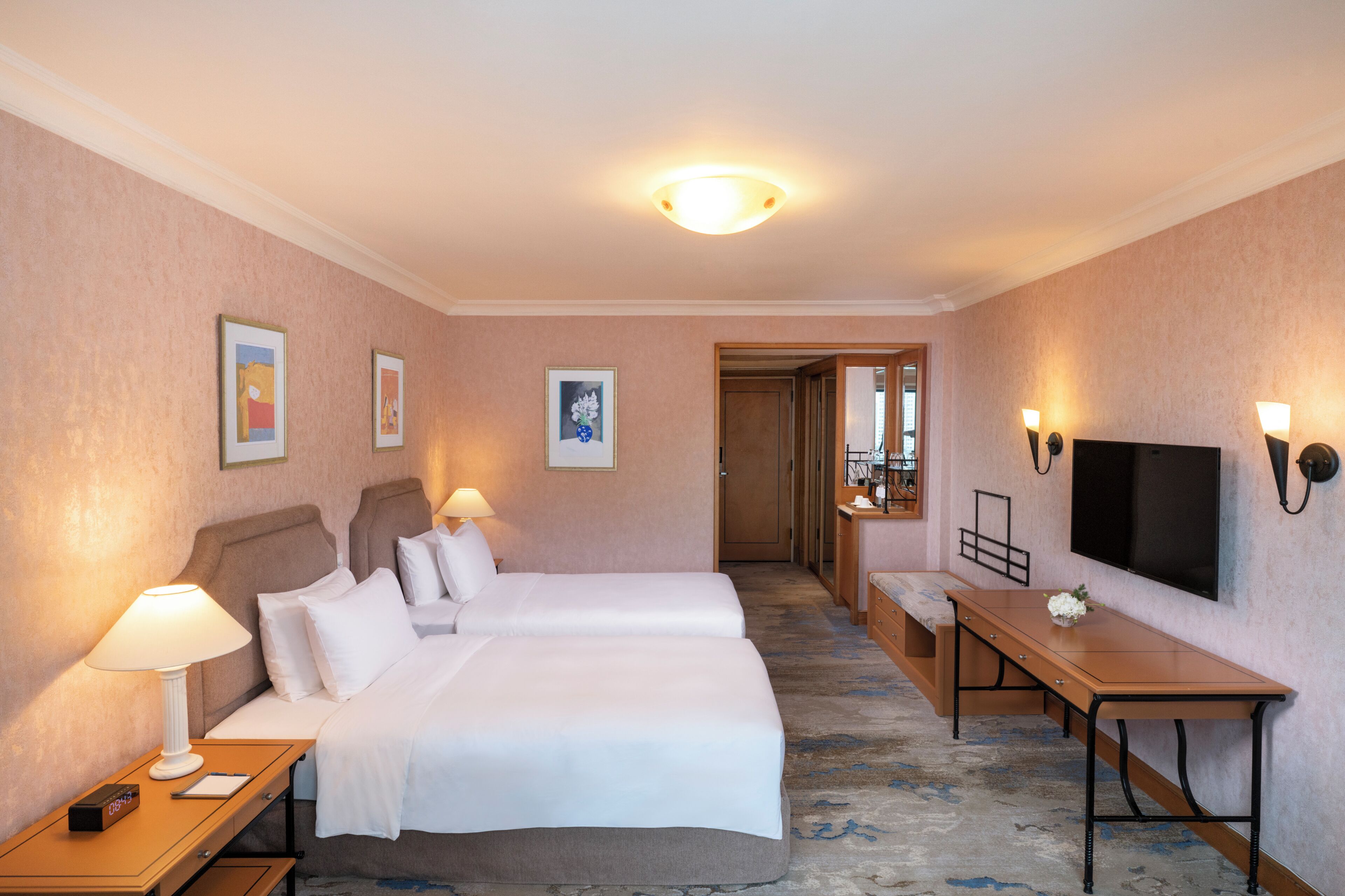 A hotel room with two beds, a desk, a TV, and a bathroom visible through an open door.