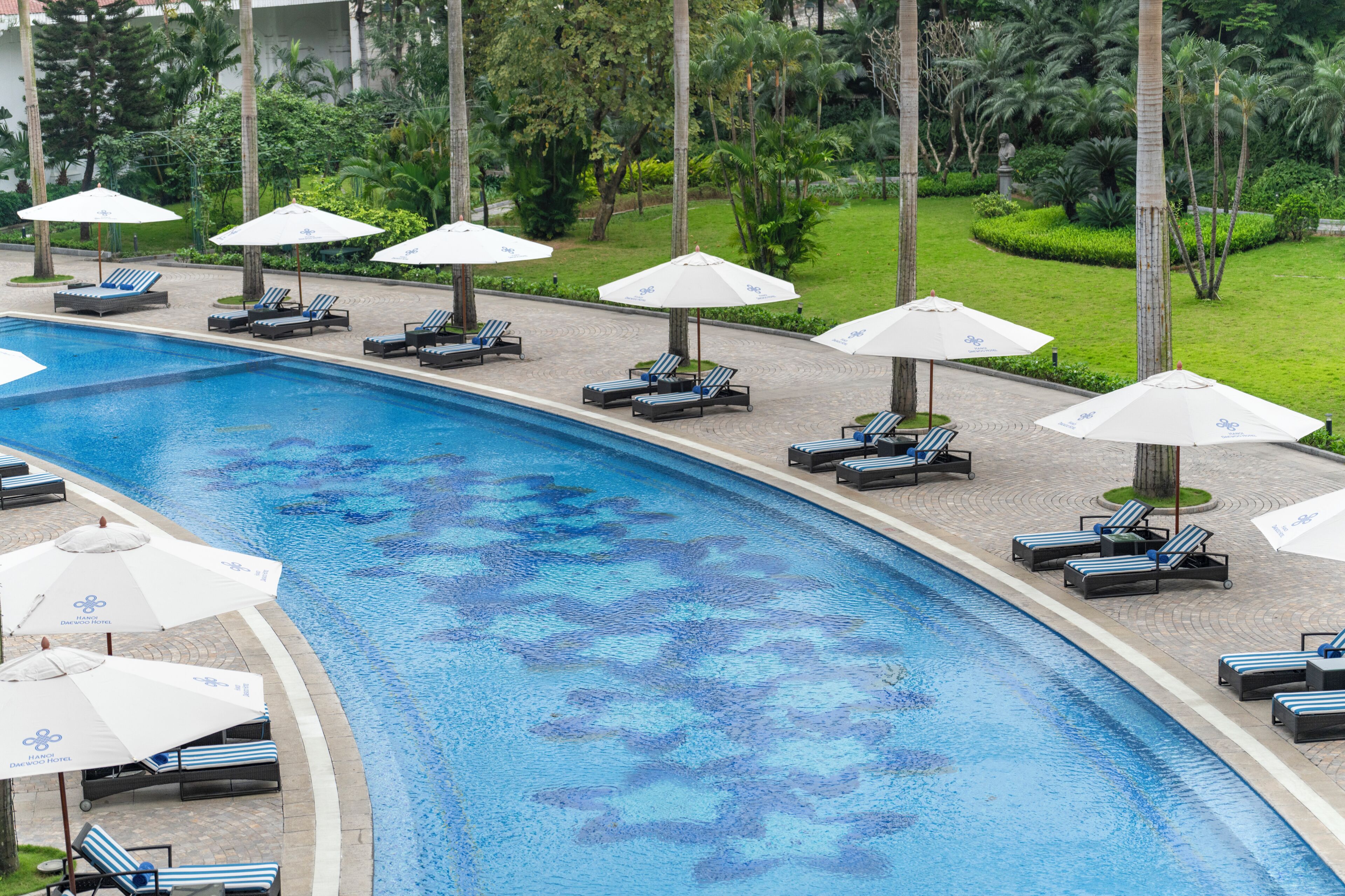 A swimming pool with lounge chairs and umbrellas, surrounded by greenery.